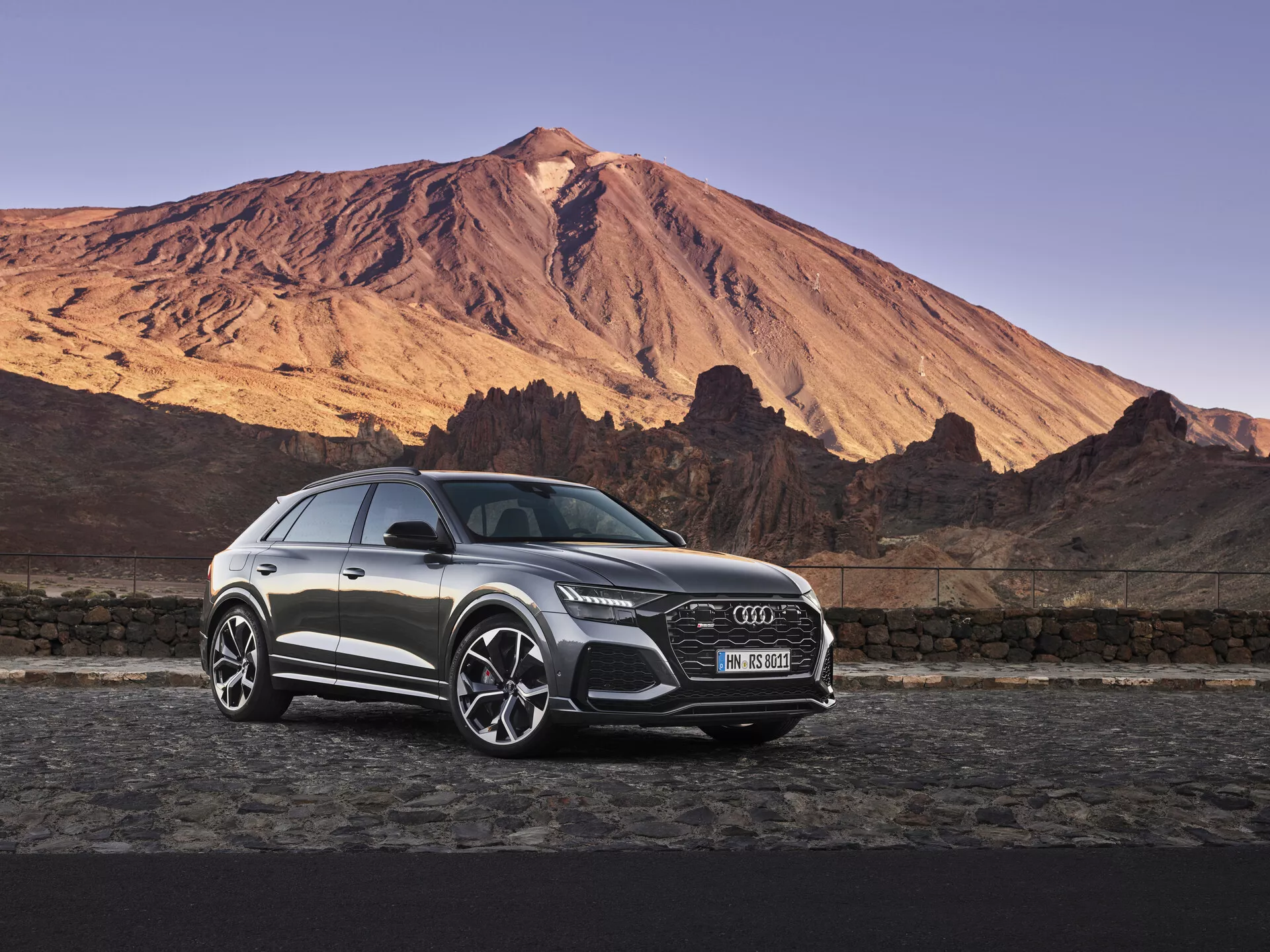 Lyxig Audi Q8 2018 SUV parkerad mot en dramatisk berglandskap vid gryning eller skymning under en klar himmel, som visar den framträdande frontgrillen, LED-strålkastarna, lättmetallfälgarna och eleganta designdetaljer i mjukt naturligt ljus.