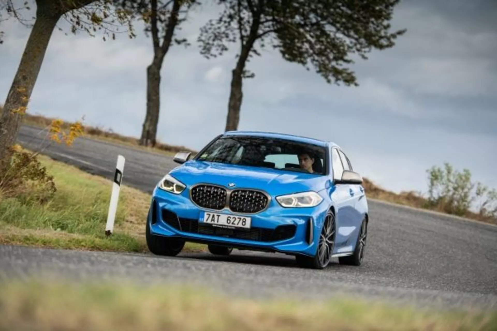 2019 BMW 1-serien M Performance blå sportssedan fångad från ett lågt och vinklat sidoframifrån perspektiv som framhäver dess aggressiva front med ikonisk njurformad grill, slanka LED-strålkastare, stora luftintag för kylning av prestanda, låg sportfjädring, i rörelse runt en kurva som visar dynamisk hantering, med aerodynamiska sidospeglar, stora legeringshjul och lågprofildäck som betonar sportig status och greppförmåga.
