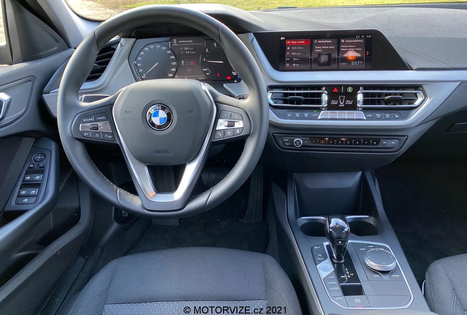 Interiörvy av en BMW 1-serie (BMW 116i) 2019 från framsätespassagerarens perspektiv, som visar den multifunktionella ratten med monterade kontroller, digital instrumentkluster, stor infotainment pekskärm, klimatanläggningssystem, automatisk växelspak, körlägesväljare och iDrive-kontrollknap.