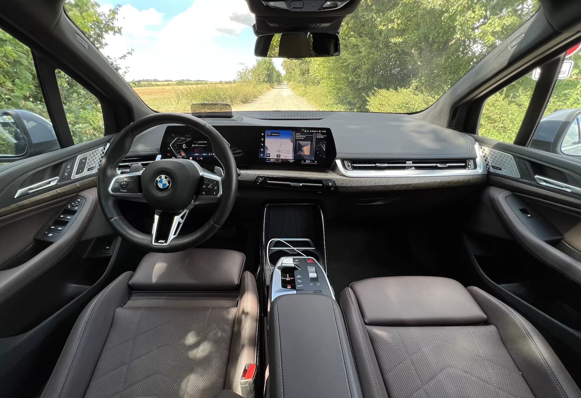 Interiör vy av en BMW 2-serie Active Gran Tourer 2022 som visar multifunktionsratten med BMW-logotyp, stor pekskärmsdisplay för infotainment, läderklädda säten och avancerade teknikfunktioner från förarsätets perspektiv.