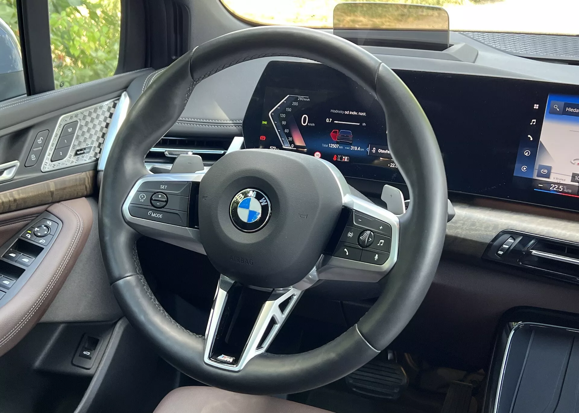 Interiörvy från förarsätet i en BMW 2-serie Active Gran Tourer 2022, fokuserad på ratten med multifunktionsknappar och högupplöst digital instrumentpanel, inramad av premiummaterial och del av infotainmentskärmen
