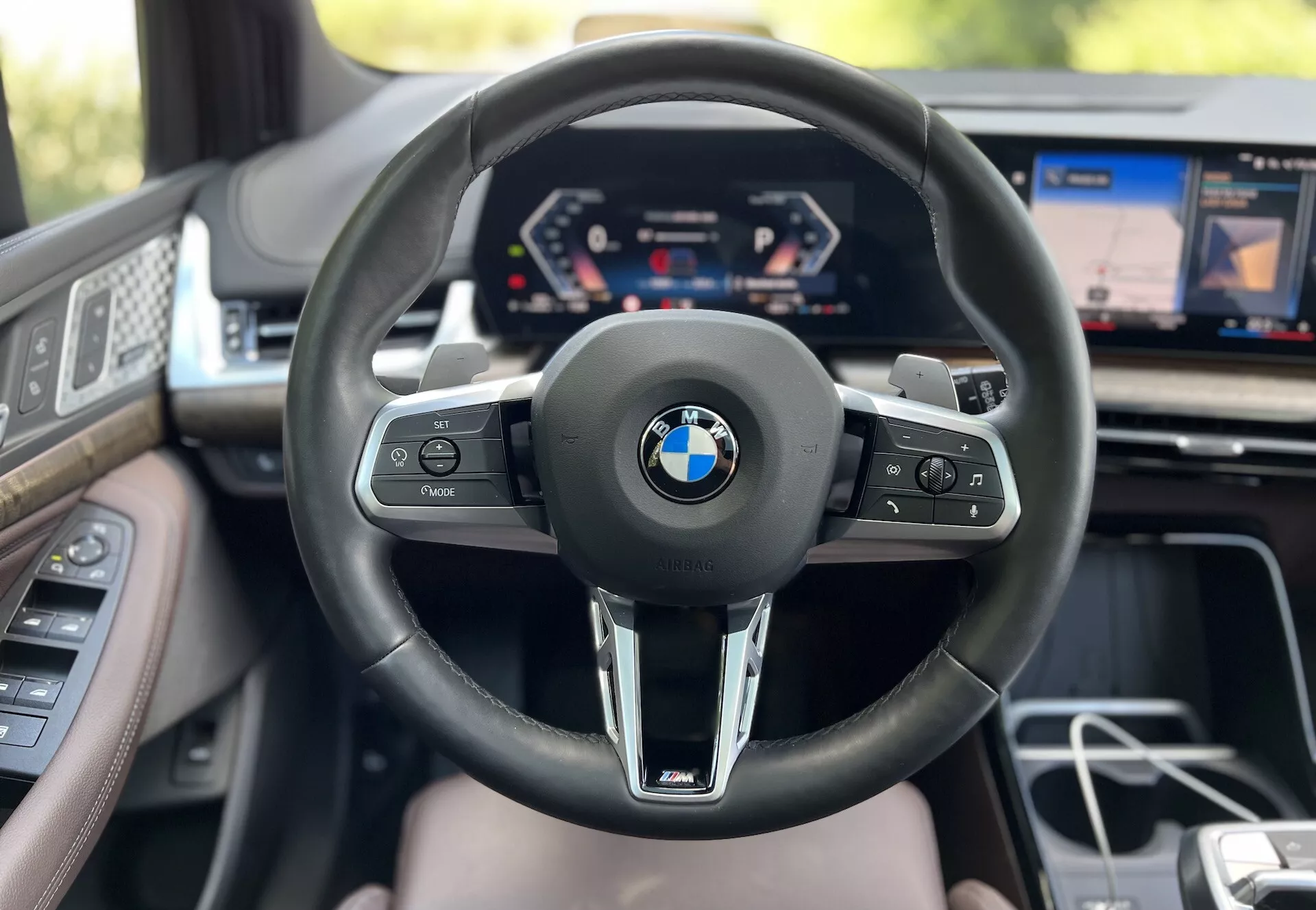 Interiörvy av BMW 2 Series Active Tourer 2022 ur förarens perspektiv med synligt styrhjul med BMW-logotyp och M-branding, digital instrumentbräda och delvis infotainmentskärm som visar avancerad fordonsteknologi och lyxfunktioner