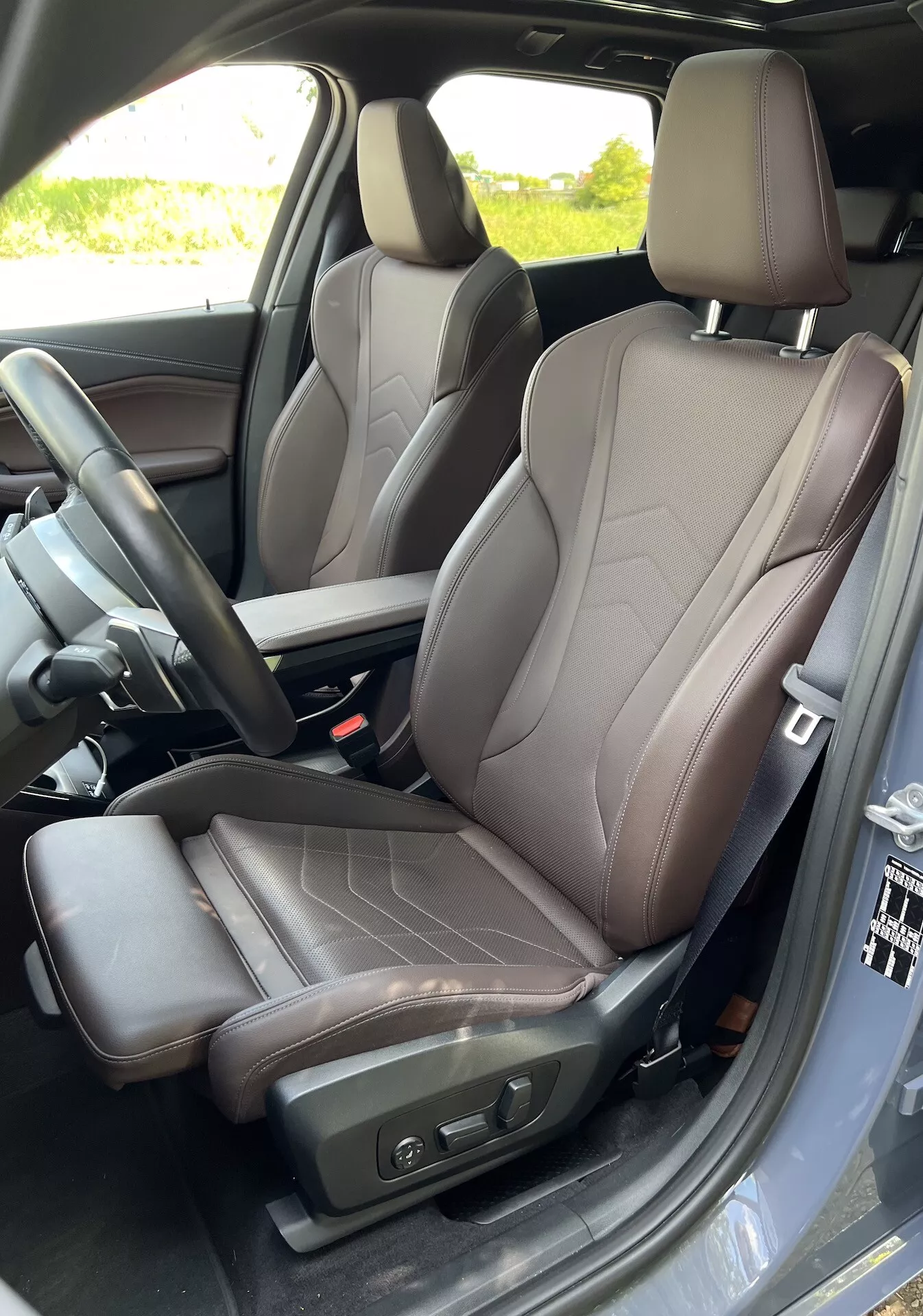 Interiörvy av förarsätet i en BMW 2-serie Active Gran Tourer 2022 som framhäver modern sättesign i tvåfärgat läder, kontroller för stolsjustering och synlig del av mittkonsolen