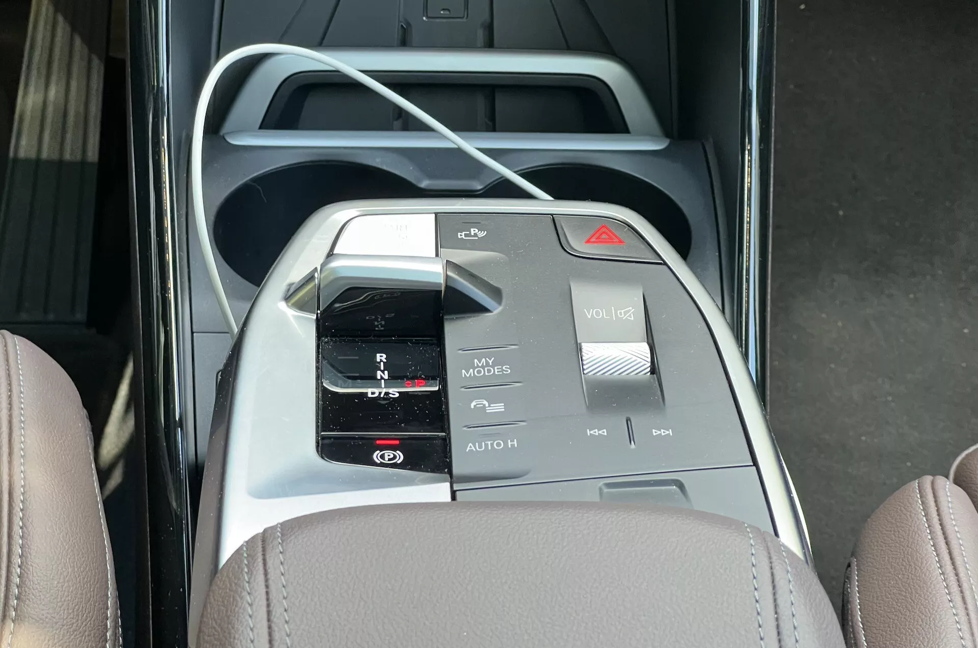 Översikt av centrala konsolen i BMW 2 Series Active Tourer 2022 med automatisk växelväljare, mugginnehavare, multimedia kontrollgränssnitt med olika knappar och strömbrytare, och tvåtonad interiör design med läder och metalliska accenter