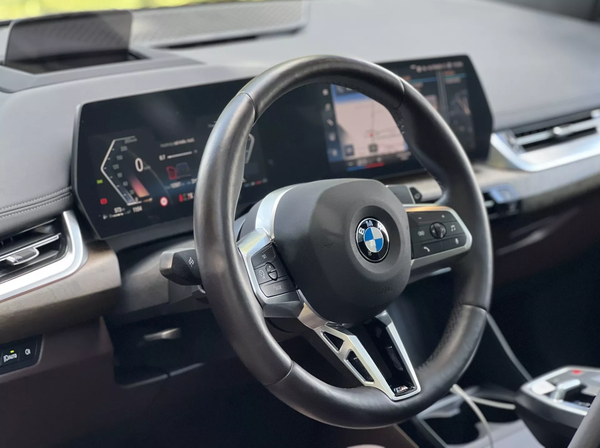Interiörbild av BMW 2-serien Active Tourer 2022: ratt med BMW-emblem och multifunktionskontroller, digital instrumentpanel och centralt infotainmentsystem med navigationssystem, från förarens perspektiv