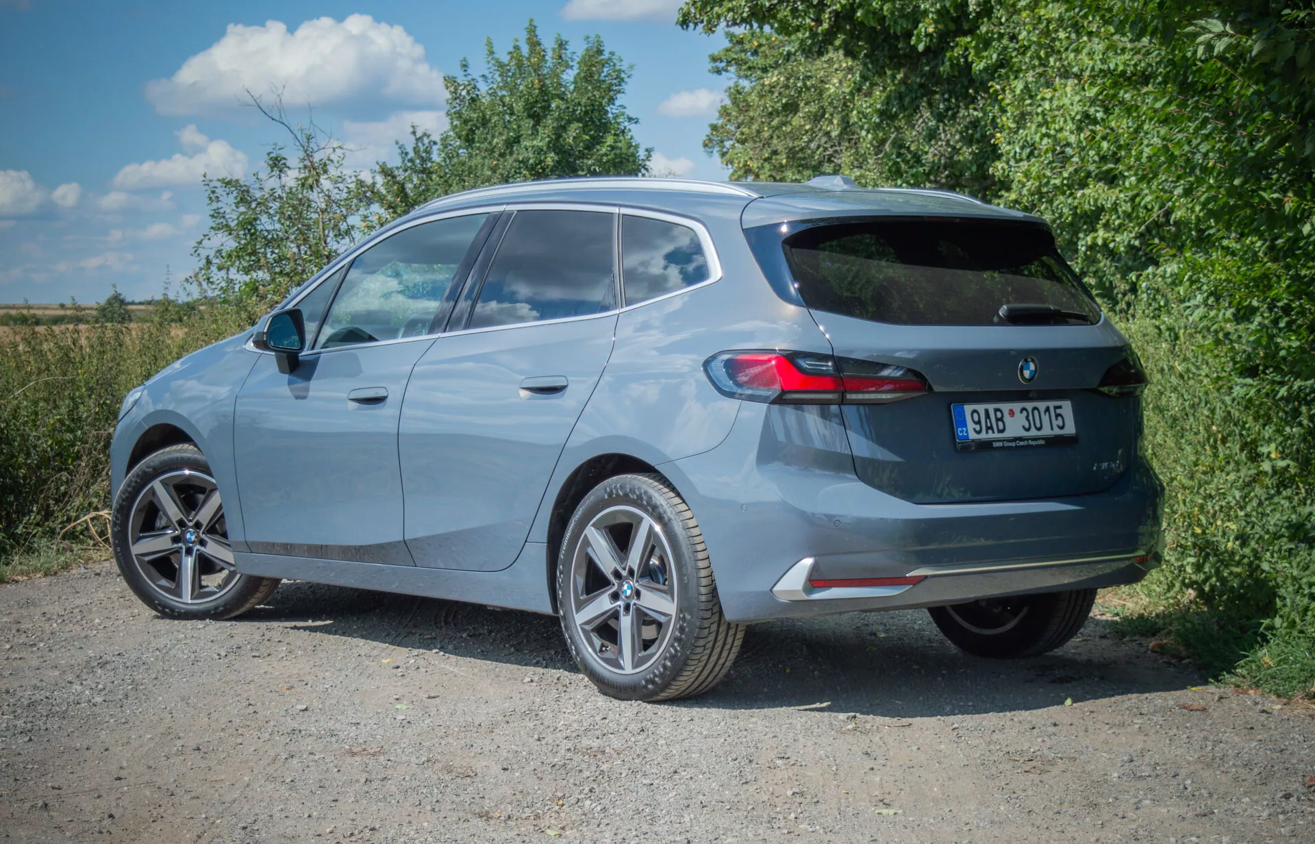 BMW 2-serien Active Tourer halvkombi 2022 i metallisk lack fångad från en tre fjärdedels bakvy, som visar legeringshjul, takspoiler, bakrutetorkare, tredje bromsljus, horisontella bakljus, enkel avgas och bakre stötfångare med integrerade reflektorer, parkerad på en opålad yta.