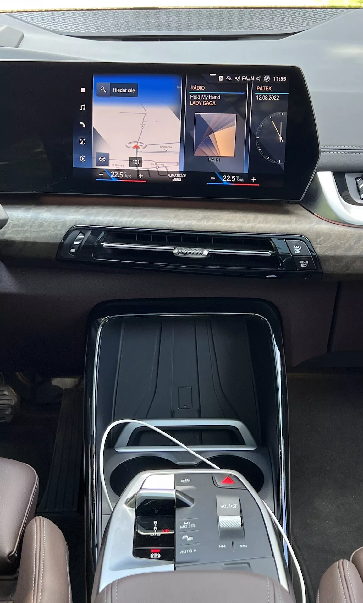 Interiörvy av BMW 2-serien Active Gran Tourer 2022 som visar mittkonsolen, widescreen touch infotainmentskärm med navigation och medieuppspelning, snygg luftventil med träimitation, klimatkontrollknappar, pekgränssnitt, elektronisk växelväljare och säten i premiumläderimitation