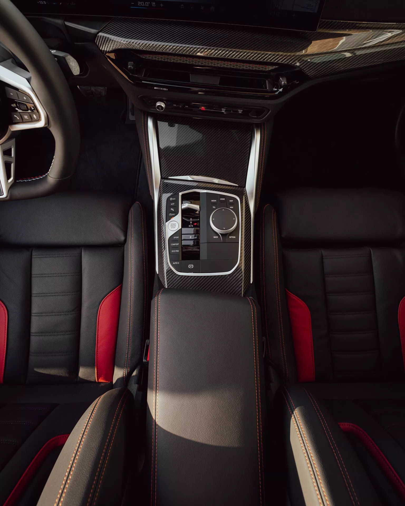Överliggande interiörvy av BMW 2-serie 2024 (G42-G87 facelift) som visar mittkonsolen med kolfiberdetaljer, elegant växelspak, elektronisk touchpad, klimatkontroller, sportiga framsäten i läder med kontrastsömmar, och partiell vy av baksätena.