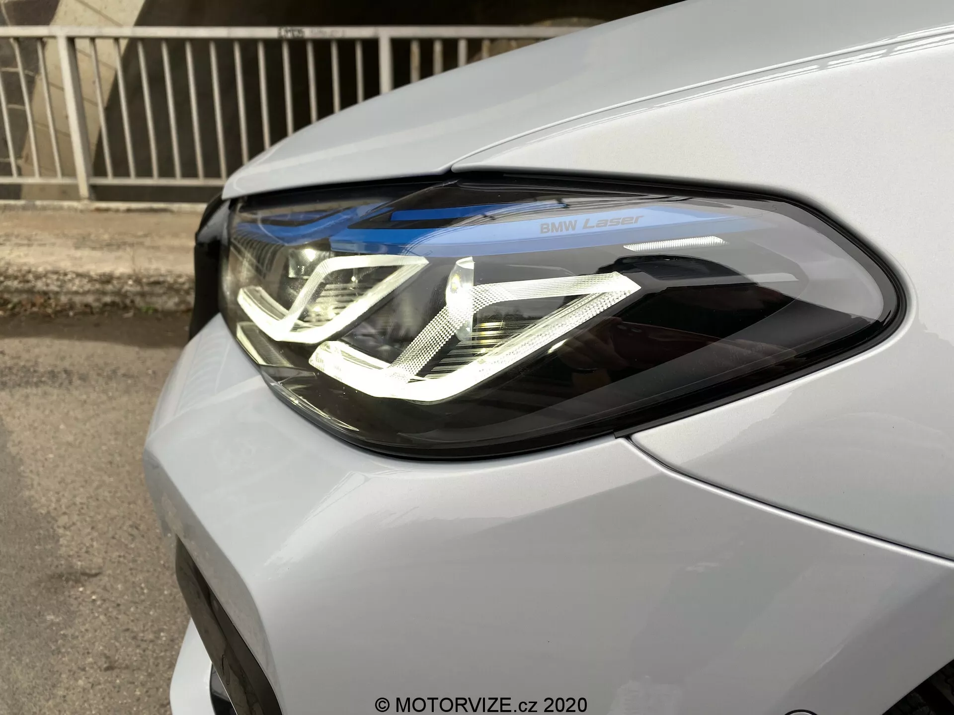 Närbild av strålkastaren på förarsidan av BMW 5-serie 2020 (BMW 520i Touring Steptronic). Bilden fångar bilen från en front-trekvartsvinkel och framhäver de intrikata LED-varselljusen med en dubbel U-form, projektorlins och inskriptionen 'BMW Laser'. Strålkastarenheten integreras sömlöst i bilens metalliska eller pärleffektlack.