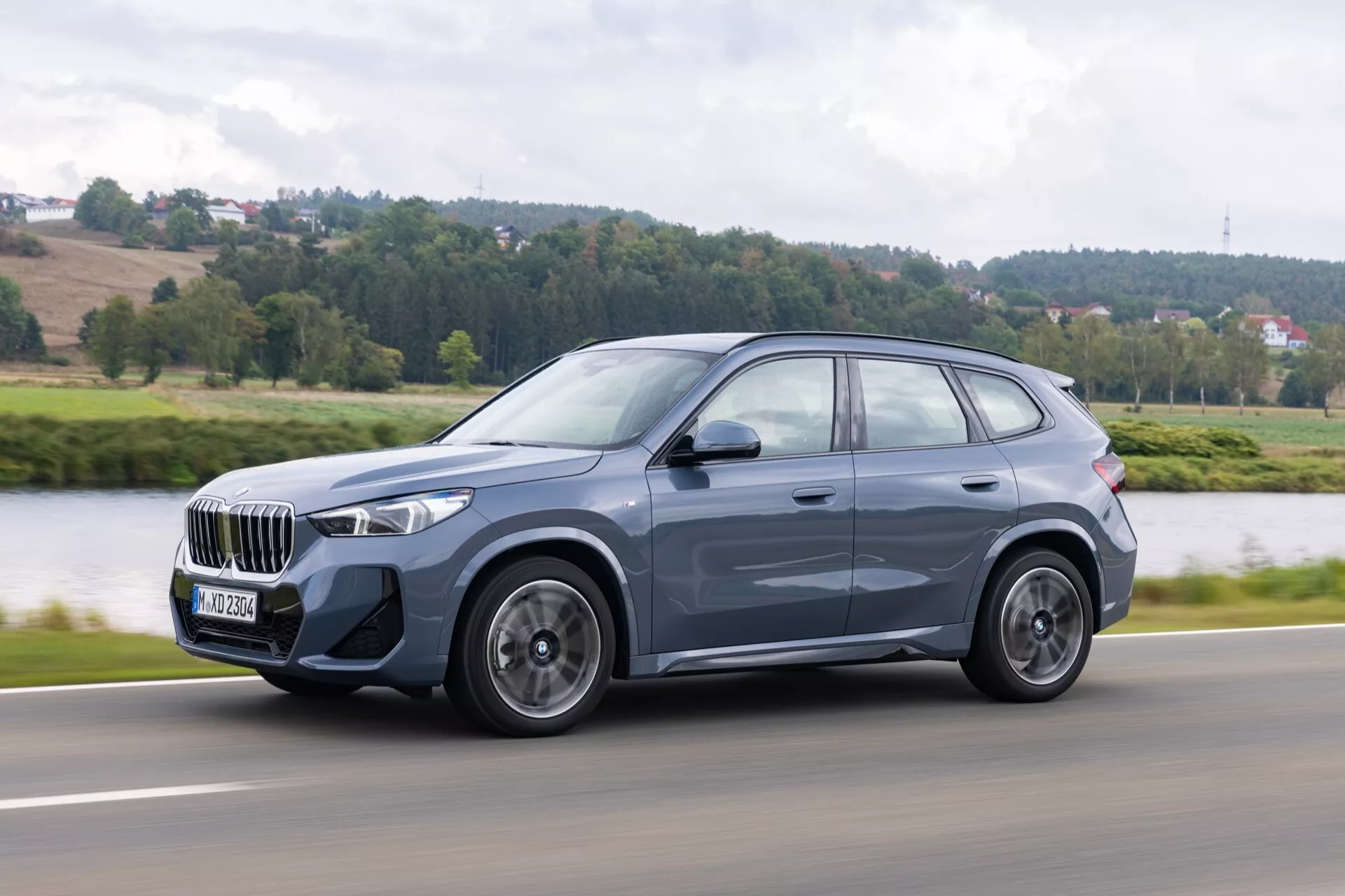 Mellanstort SUV BMW X1 (U11) 2022 i rörelse, sidoprofilvy som framhäver dynamisk silhuett, LED-strålkastare, femekrade aluminiumsfälgar, coupé-liknande taklinje, takräcken och integrerade blinkers