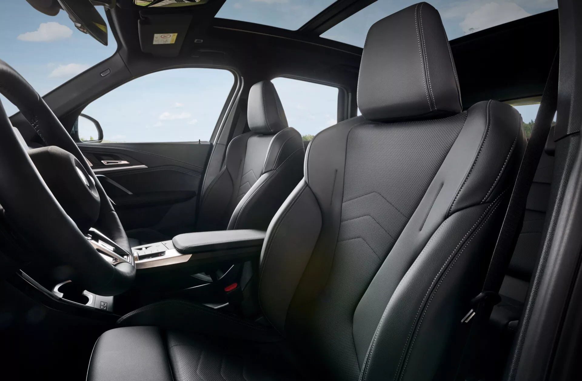 Interiörvy av BMW X1 (U11) 2022 som visar det moderna främre kupén från ett framifrån sidoperspektiv, framhäver passagerarsätet klätt i läder med geometrisk sömnad, snygg mittkonsol med växelspak och klimatkontroll, minimalistisk instrumentbräda och potentiellt soltak för en känsla av lyx