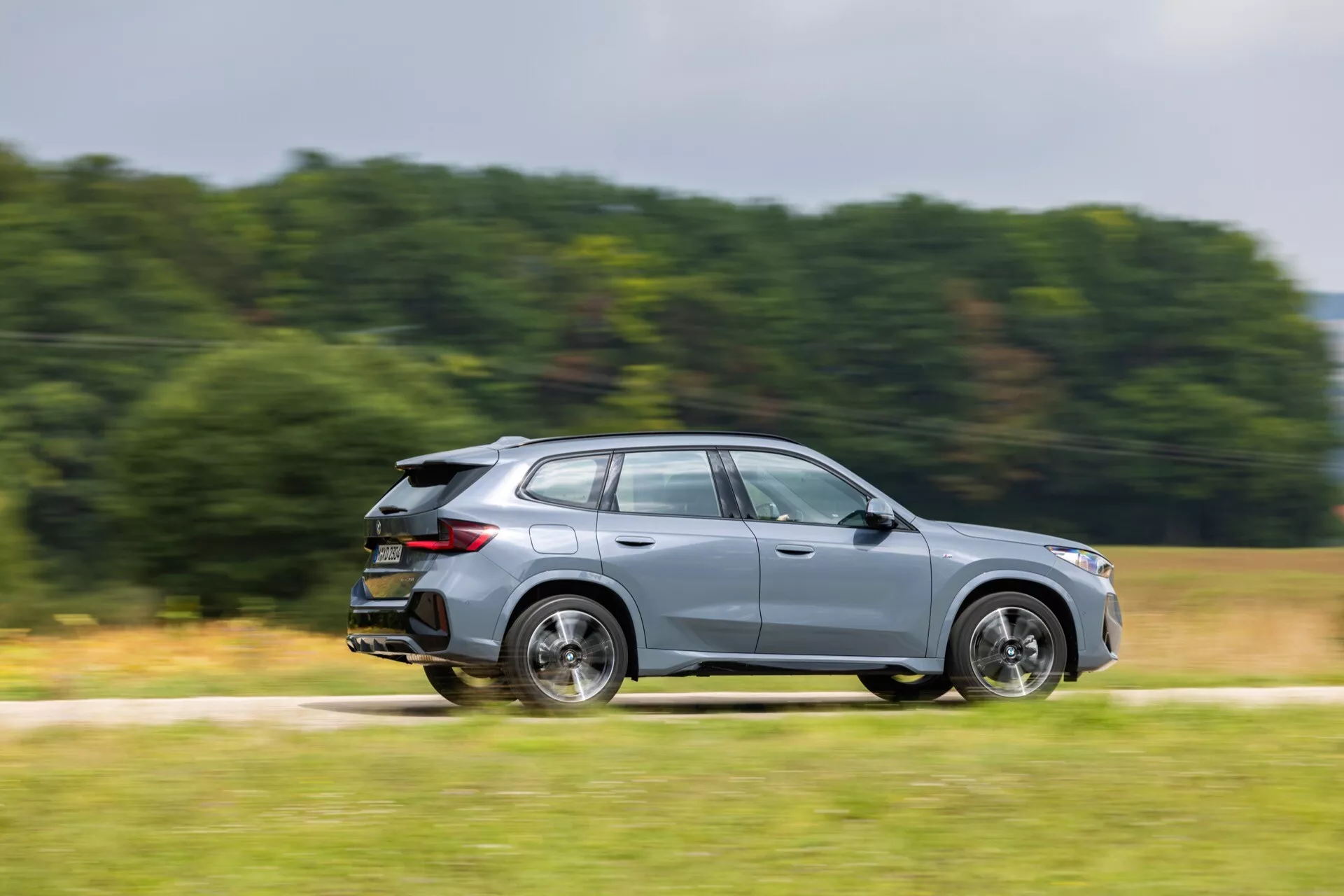 BMW X1 (U11) 2022 i rörelse med sidoprofil, ljusa LED-strålkastare, elegant aerodynamik, flerspakiga aluminiumfälgar och integrerad bakspoiler, belyst med panorering fotograferingsteknik.