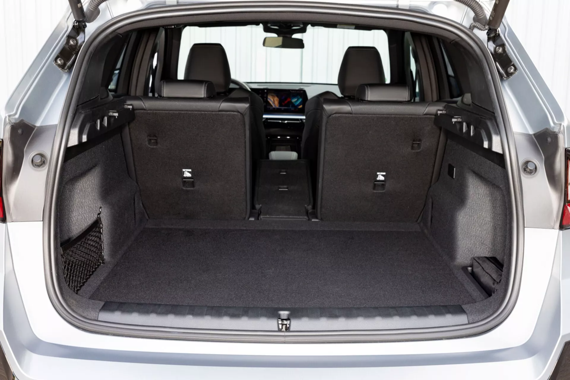 Vy över lastutrymmet i BMW X1 (U11) 2022, med rymligt utrymme klätt med matta, platt nedfällbara baksäten, integrerade krokar, LED-belysning, 12V-uttag och ett infällbart privat skydd, designat för förbättrad flexibilitet, bekvämlighet och säkerhet för lasten