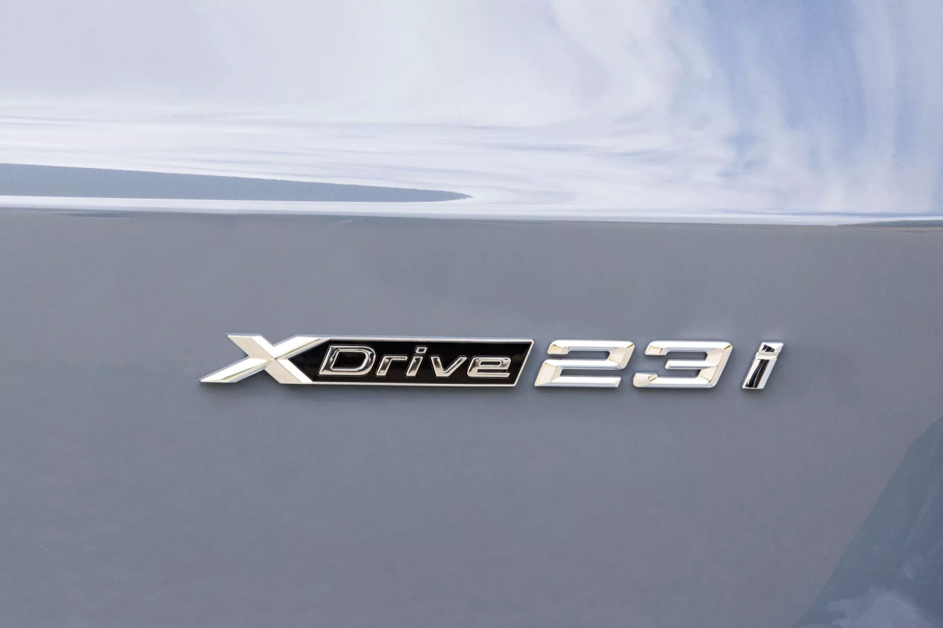 Närbild av BMW X1 2022 (U11) XDrive 23i metall emblem på bakluckan, med krom bokstäver mot en mörkgrå, blank bilkaross