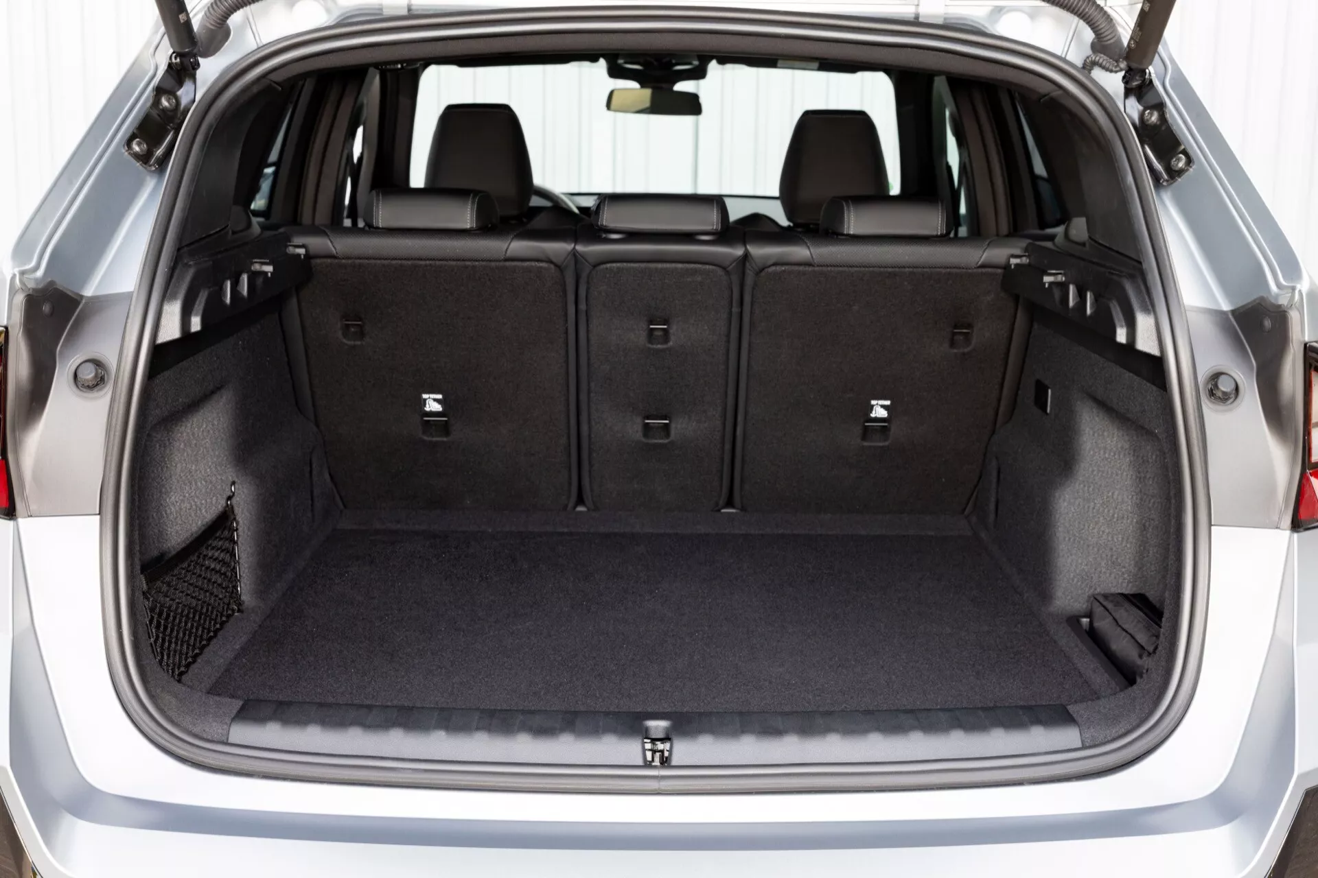 Detaljerad vy av BMW X1 2022 (U11) bakre bagageutrymme som visar rymlig förvaringsutrymme, mattbelagt golv, fällbara baksäten, inre belysning, surrningpunkter, slitstarka sidomaterial, eluttag och säkerhetsnödfrigöringsfunktion