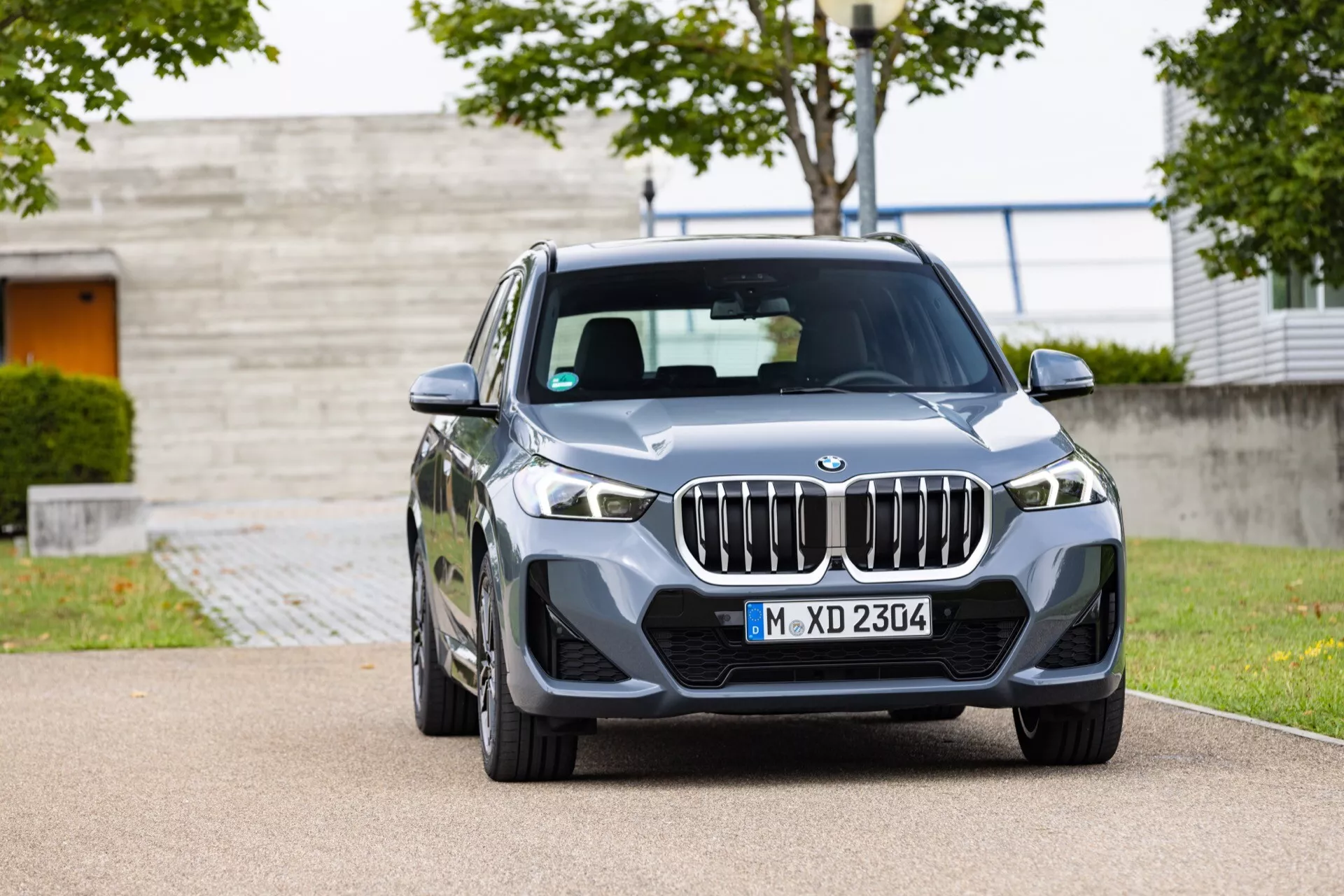 BMW X1 (U11) från 2022 visar upp sin lyxiga metalliska blå fasad, med en kromad njurformad grill, slanka vinklade LED-strålkastare, konturerad huva, sportig frontstötfångare med stora luftintag och legeringshjul i en detaljerad frontvy som betonar fordonets avancerade teknik och eleganta design.
