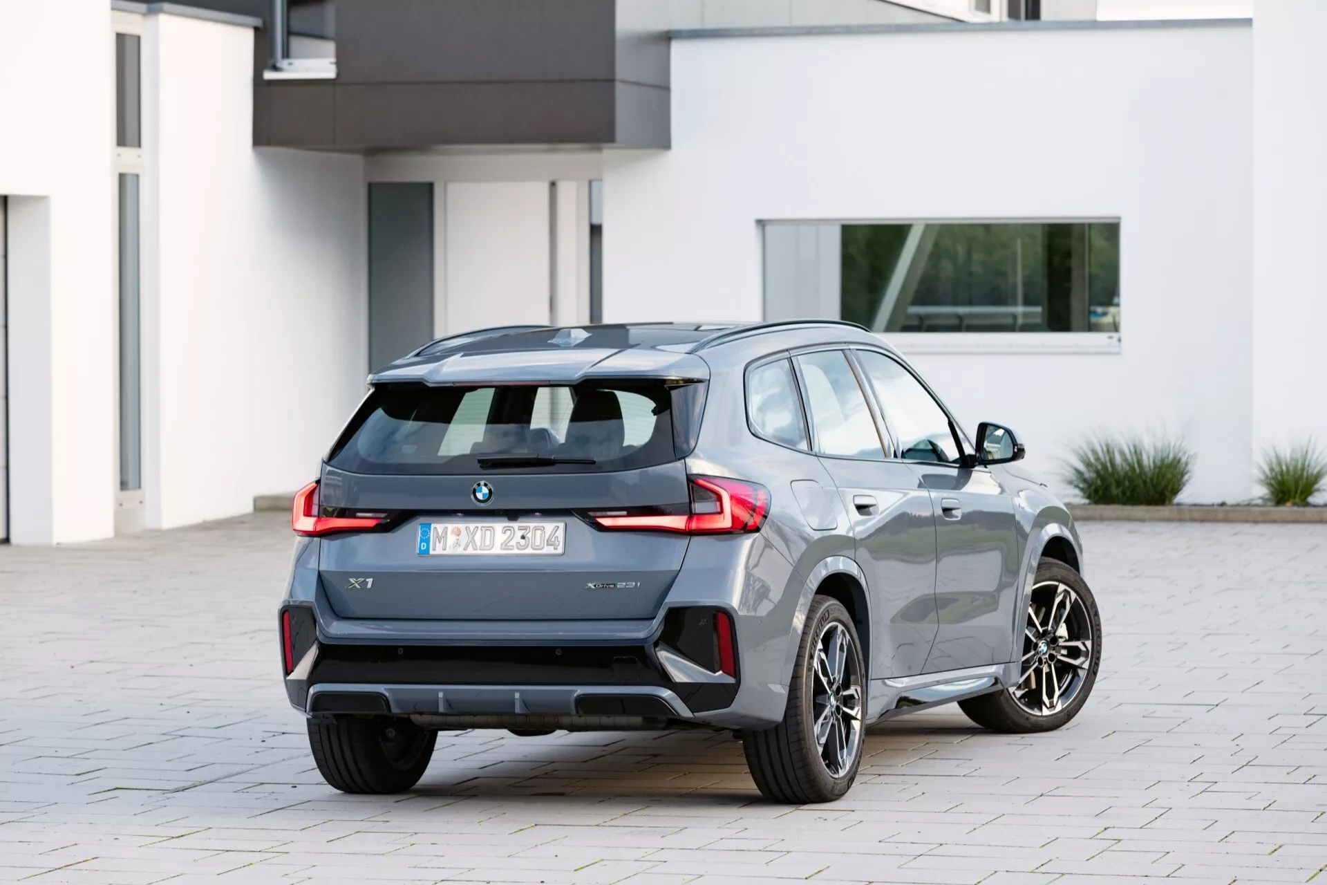Modern halvkombi BMW X1 (U11) 2022 fångad från ett bakåt-tre-kvarts perspektiv som visar sidoprofil och baksida med distinkta bakljus, dubbla avgassystem, legeringshjul och potentiella parkeringssensorer
