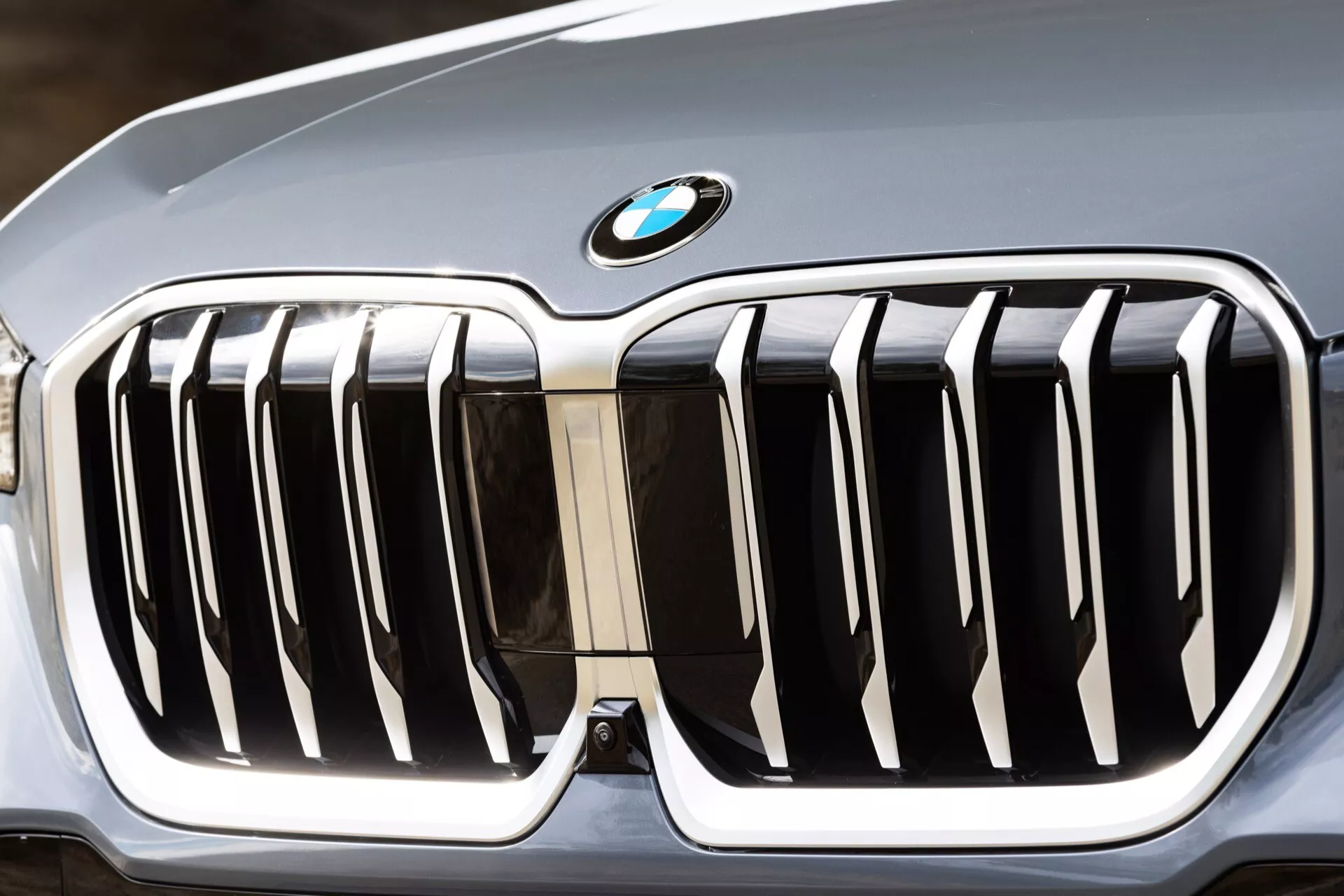 Närbild av frontgrillen på BMW X1 (U11) 2022 som visar den signatur BMW njurgrillen med kromslitsar mot en blank svart bakgrund, toppad med den ikoniska blå och vita BMW-logotypen