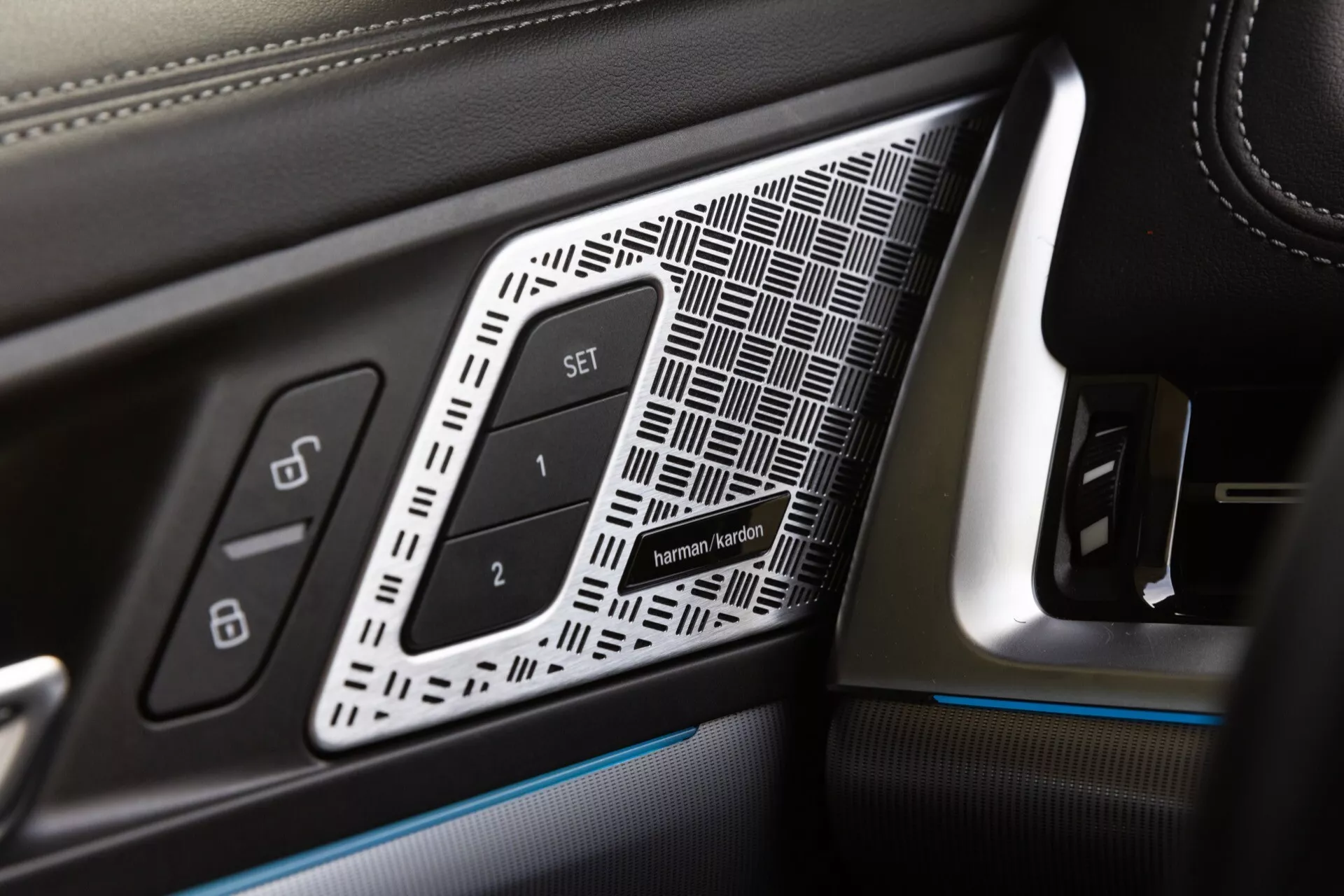 Närbild på förarsidans dörrpanel i en 2022 BMW X1 (U11), med lyxiga detaljer som läder med kontrastsöm, geometrisk insats, minnessätesknappar och omgivningsbelysning