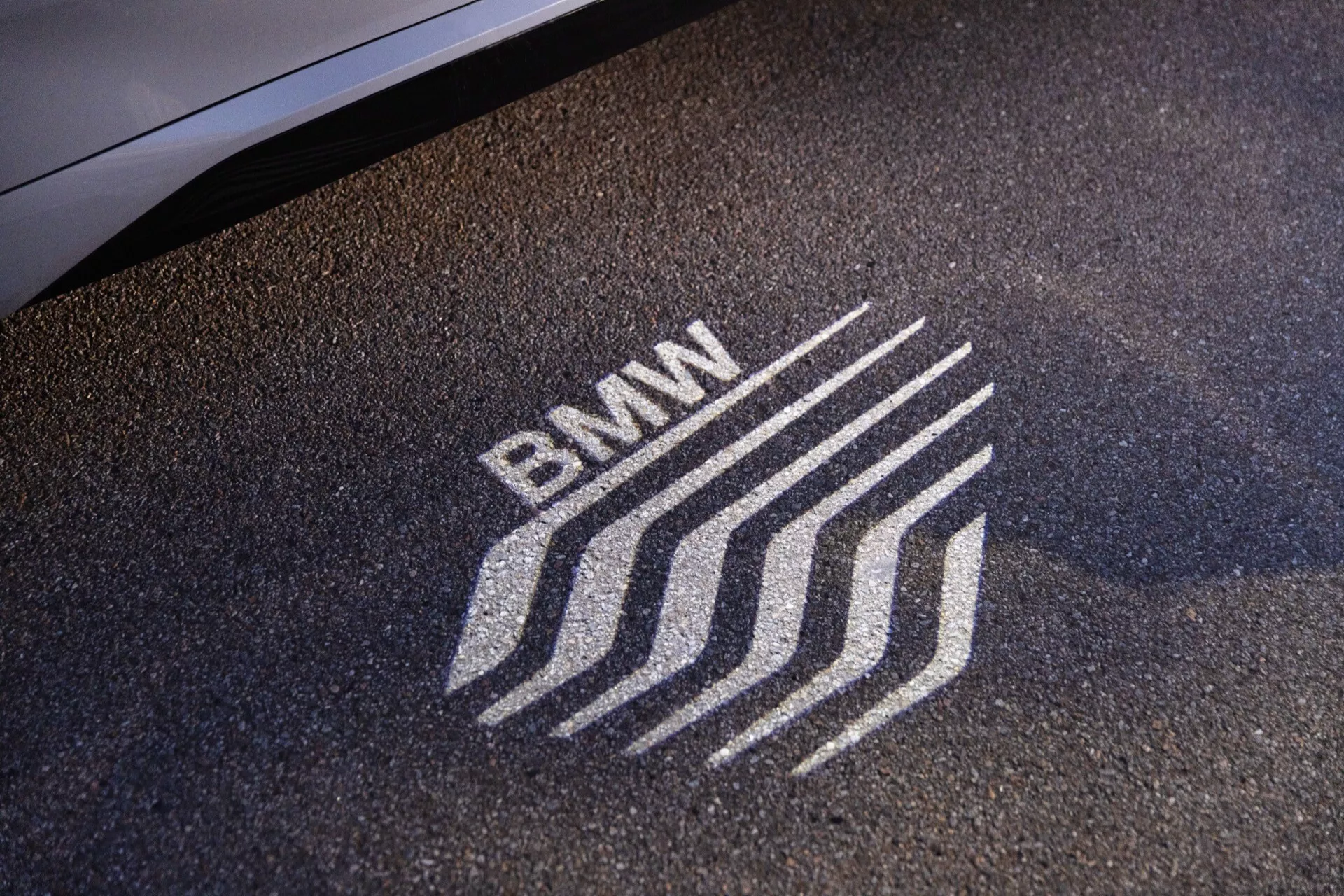 Närbild av BMW-logotypens projektion på marken från en pöl-ljus på en BMW X1 2022 (U11), som visar avancerad bilsteknologi för belysning och lyxbranding.