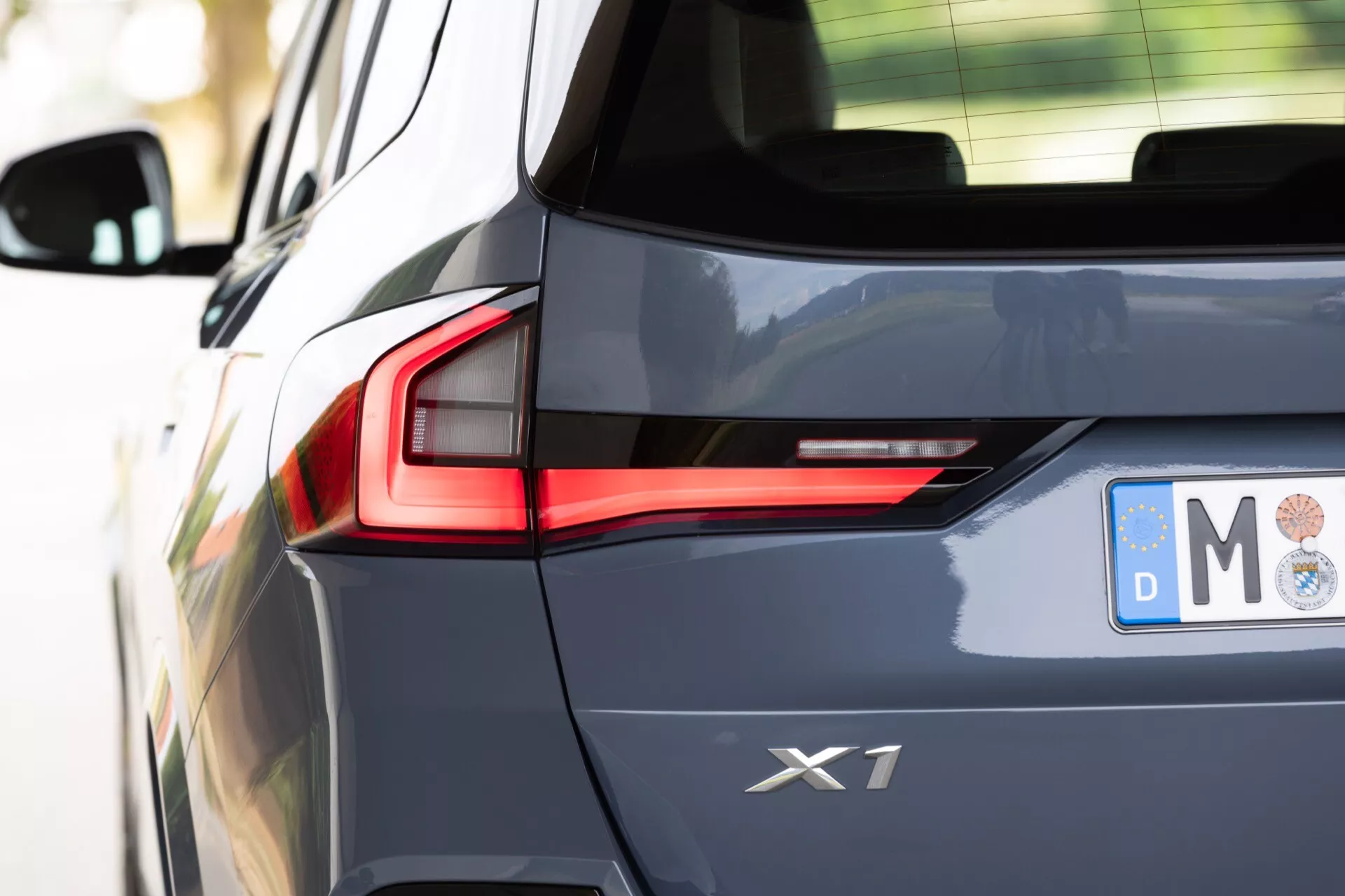 Närbild från sidan av en BMW X1 2022 (U11) som visar bakre kvartsdesign, emblem, höger bakljus med röd LED-signatur, bakre stötfångare och en del av bagageluckan. Marknivåbilden fokuserar på premiumfordonets moderna belysning och mörka metalliclack.