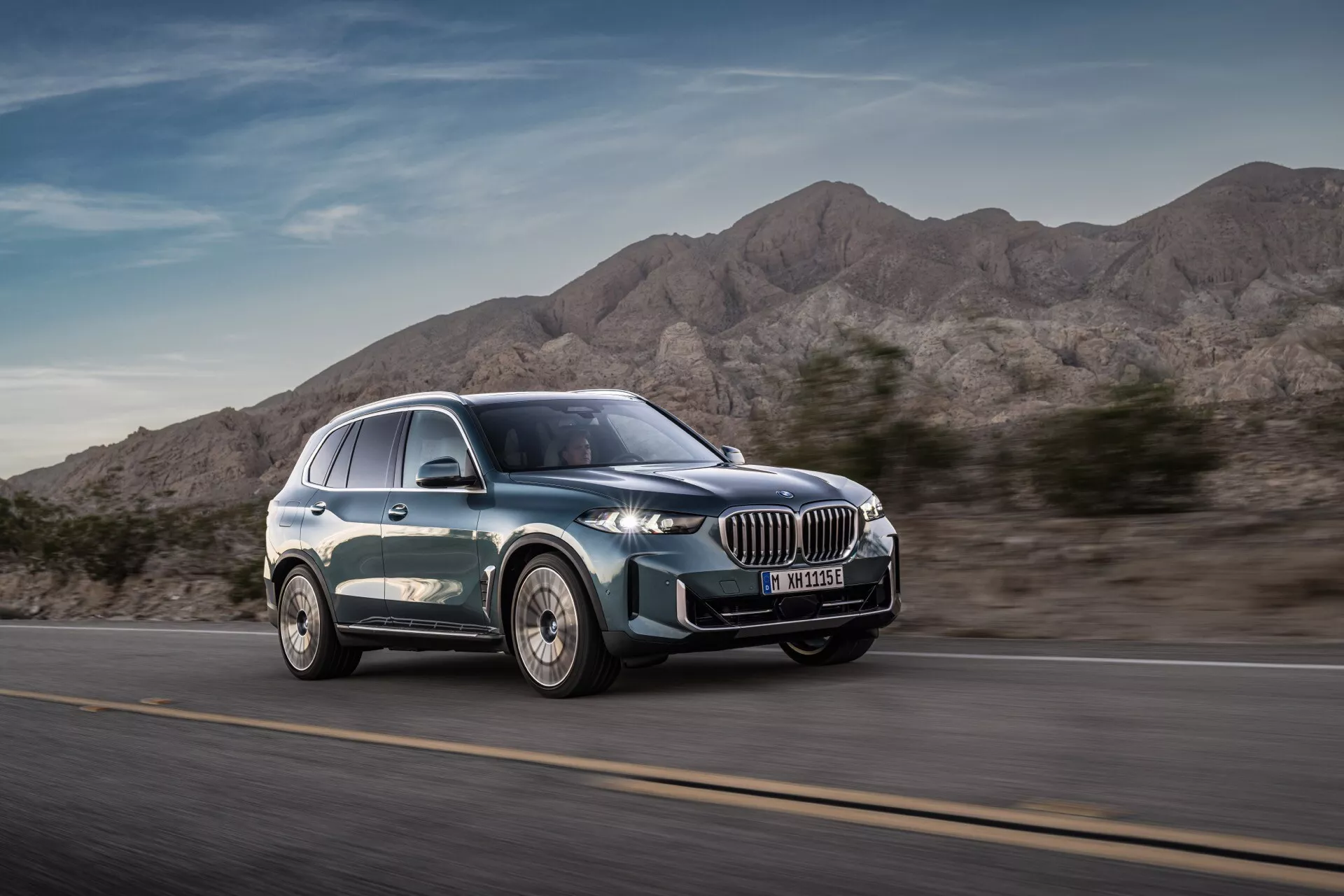 Modern lyx SUV BMW X5 2023 (G05-F95 Facelift) i rörelse från ett trekvarts frånvinkel som framhäver dynamisk design, stor njurformad grill, smala LED-strålkastare, flerkantiga lättmetallhjul och slät silhuett med metallisk lack