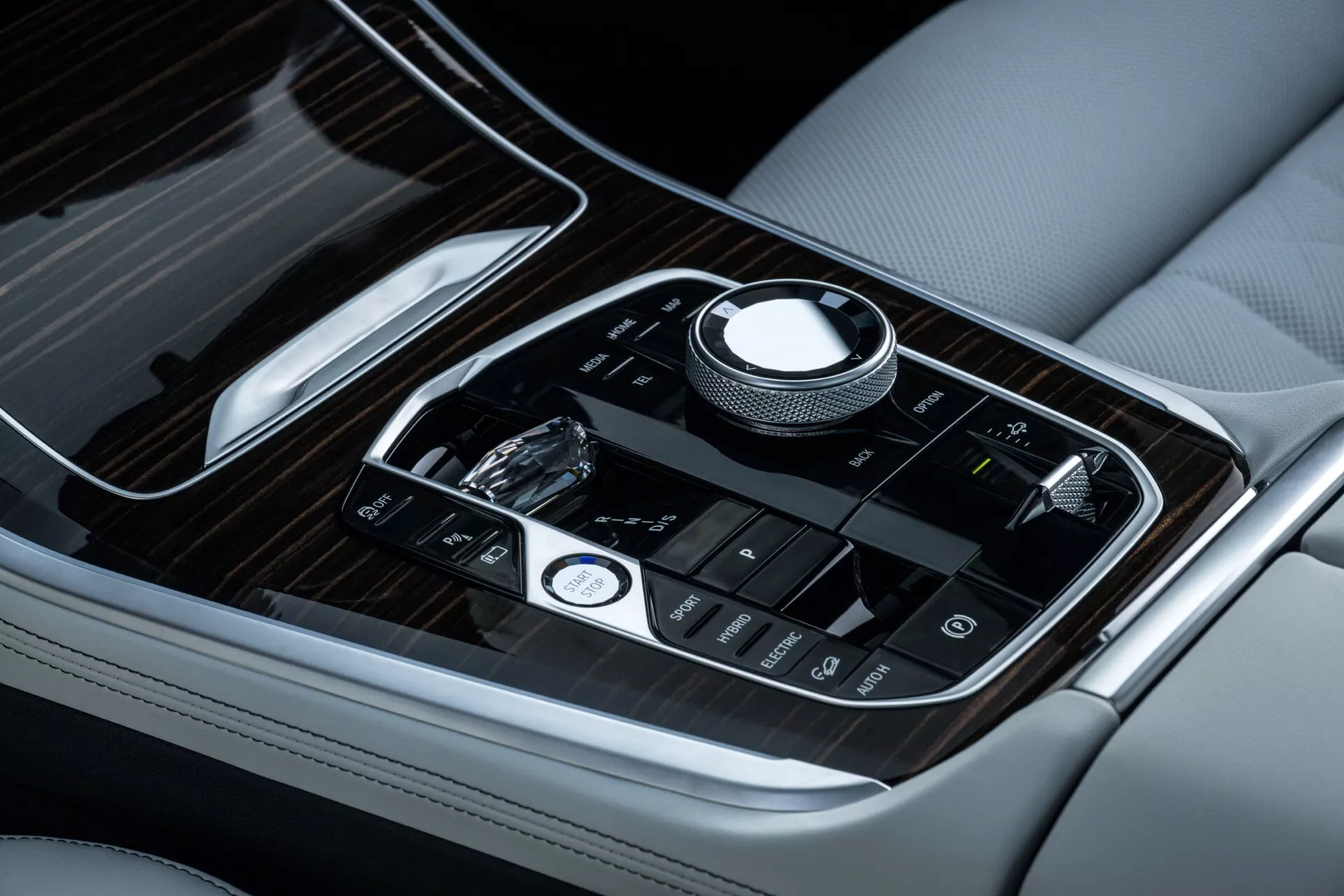 Närbild av mittkonsolen i BMW X5 2023 (G05-F95 Facelift) som visar lyxigt läder med kontrastsömmar, trädetaljer och avancerade pekkänsliga kontroller med roterande ratt för multimedienavigation
