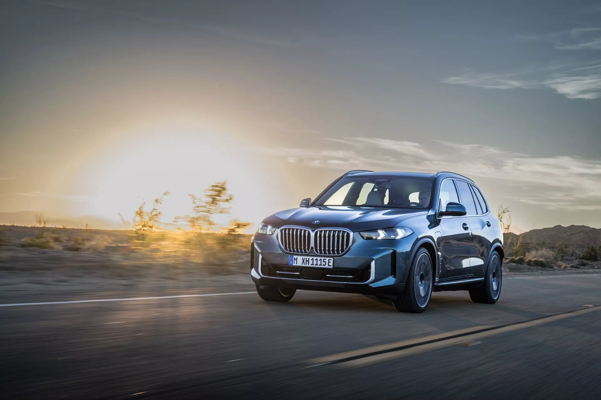 BMW X5 2023 (G05-F95 Facelift) i Rörelse: Dynamisk Vy från Låg Vinkel som Framhäver LED-strålkastare, Legeringshjul och Aerodynamisk Design mot en Solnedgång