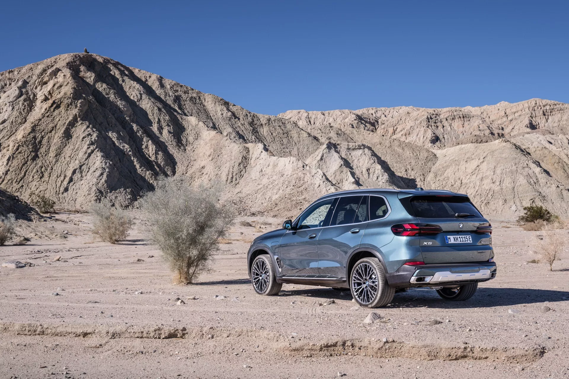 Sidoprofil av BMW X5 (G05-F95) facelift-modellen 2023 mot en naturlig ökenlandskap, med LED-belysning, aerodynamisk design, avancerade hjul- och avgassystem samt möjliga parkerings- och suspensionsteknologier.