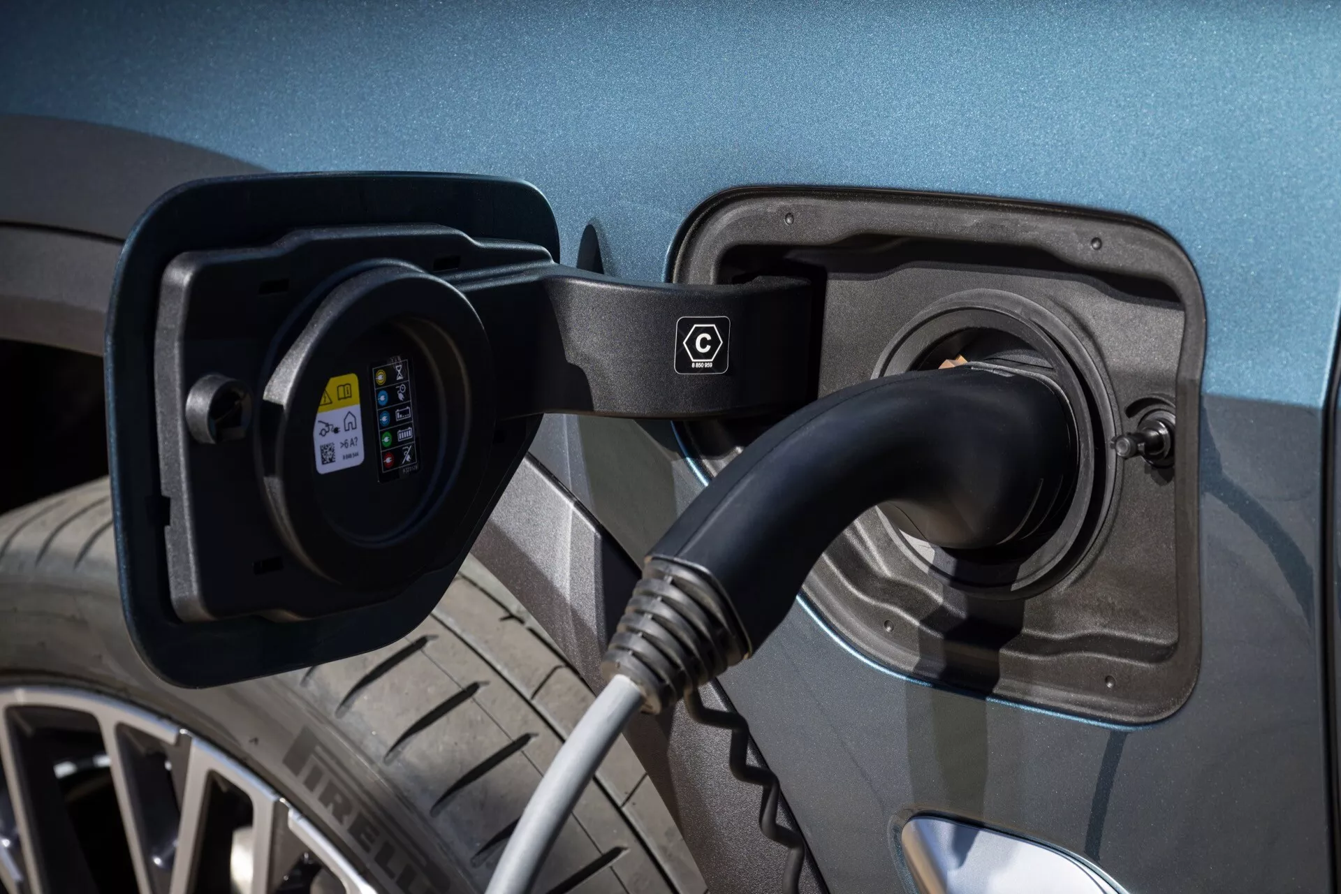 Elbil BMW X5 2023 (G05-F95) med öppen laddningsport och ansluten EV-laddningskabel och plugg, synlig laddningsstatusindikator och detaljerad vy av metallisk lack, legeringshjul och däckmönster i en välbelyst miljö som betonar modern hållbar transportteknologi.