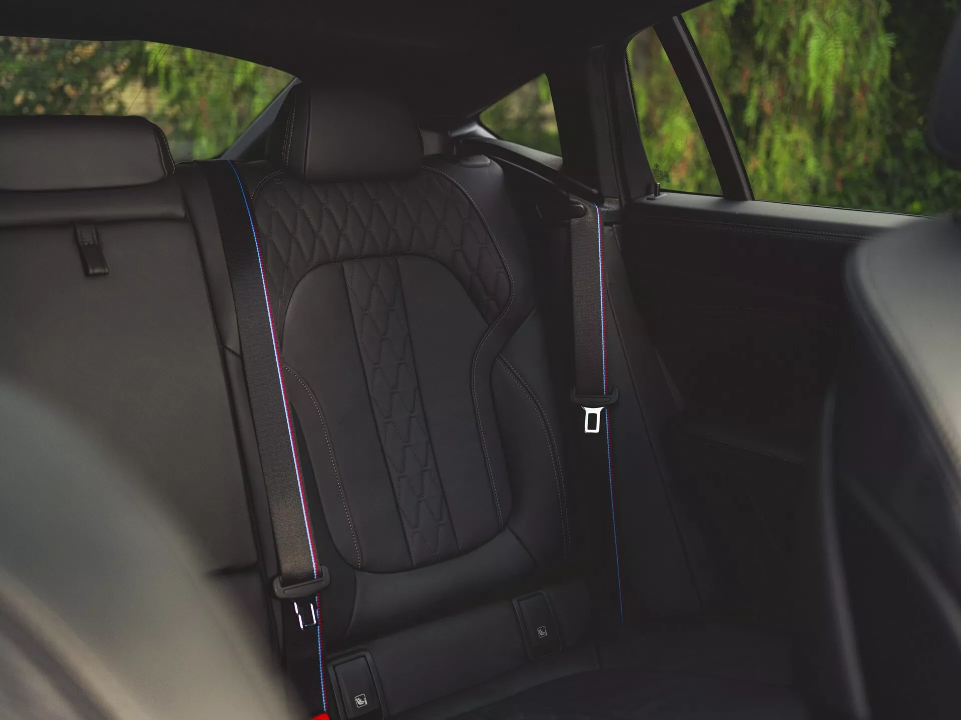 Interiörvy av BMW X6 2023 (G06-F96-Facelift) med fokus på bakre säten i premiummaterial med diamantsöm och kontrastpiping samt en glimt av säkerhetsbälteslåset som indikerar säkerhetsfunktioner, visar upp designelement av lyx och komfort.