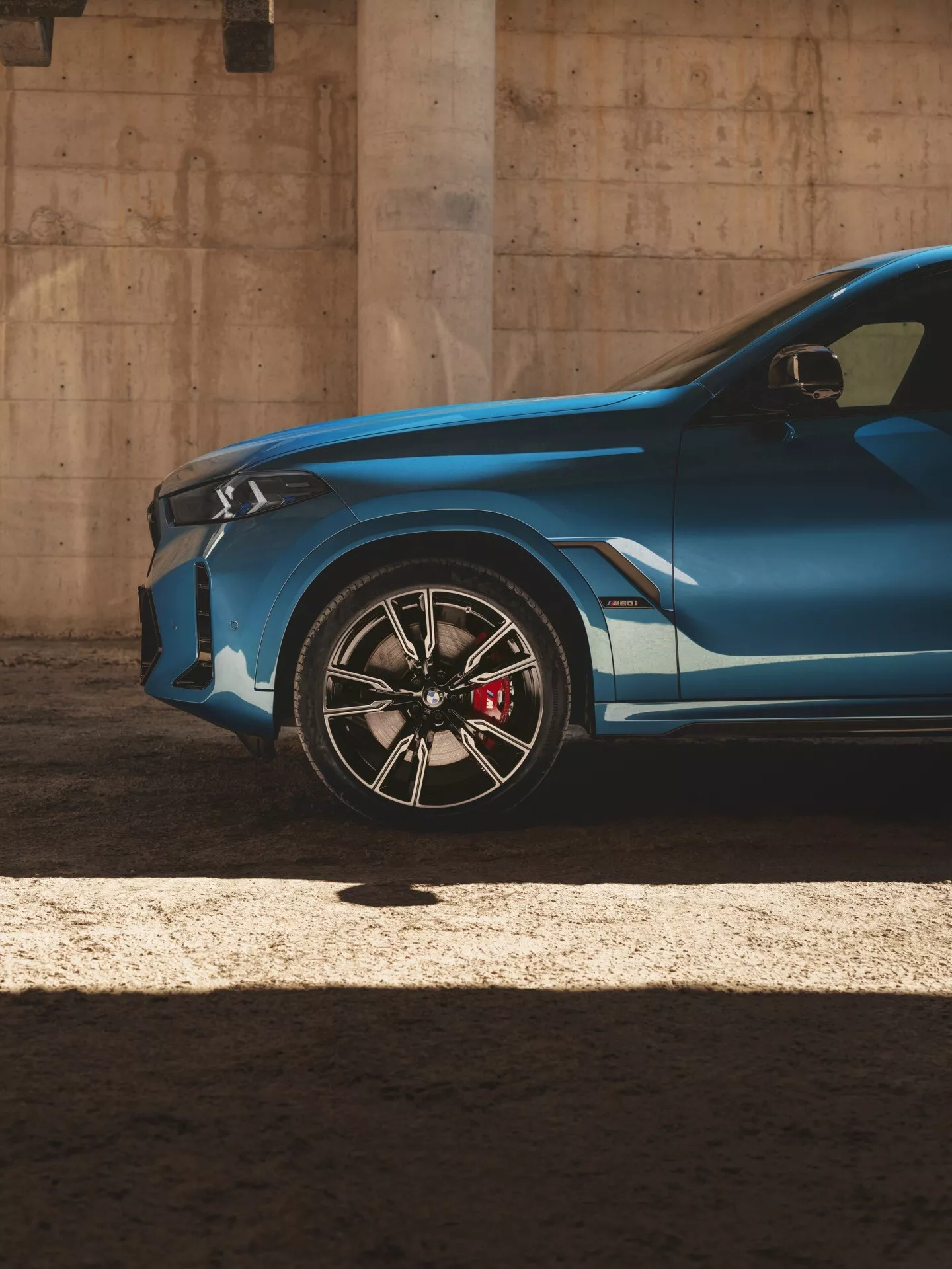 Partiellt främre höger kvartsikt av BMW X6 2023 (G06-F96-Facelift) som visar dess moderna aggressiva design, framhävd av en skarp karaktärslinje, sportig legeringshjul med en högpresterande röd bromsok, och lågprofildäck, under dramatiskt solljus som skapar högkontrast skuggor och höjdpunkter.