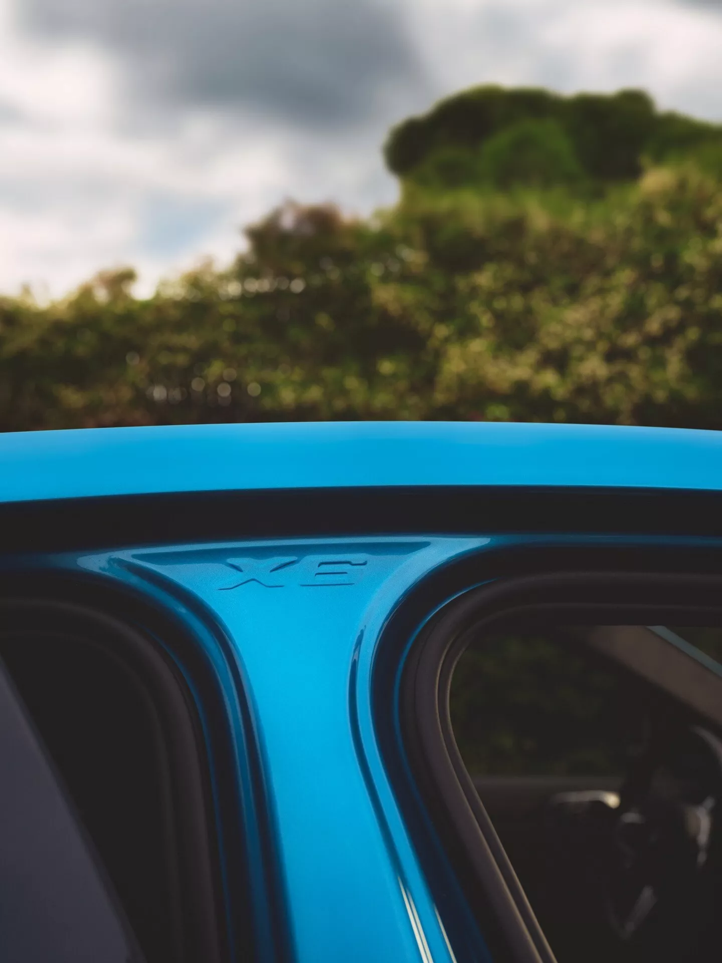 Närbild i vinkel av 2023 års BMW X6 (G06-F96-Facelift) tak med panoramasoltak med skjutfunktion och vindavvisare, svart ram mot blått, integrerade takräcken och XE-modellbeteckning