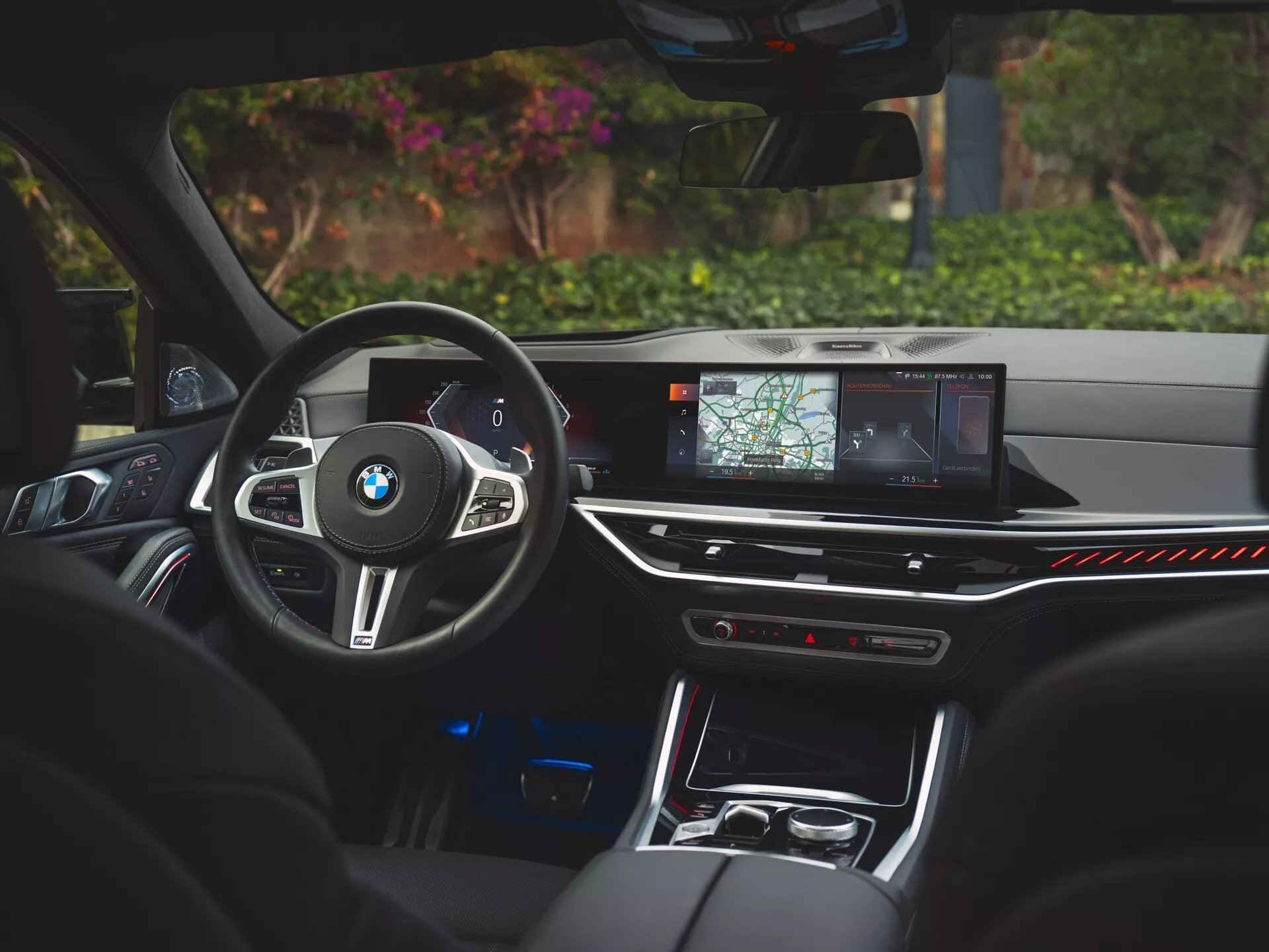 Interiörvy av BMW X6 2023 (G06-F96-Facelift) från förarens perspektiv som framhäver sportratten i läder med kontroller, högupplöst infotainment-skärm med navigation, lyxig omgivningsbelysning och premiumlädersäten