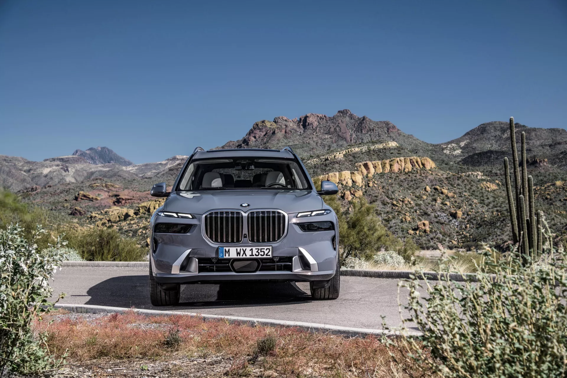Lyx-SUV BMW X7 2022 (G07-Facelift), som visar en modern design med ett stort njurformad grill, smala LED-strålkastare, avancerad frontstötfångare med ADAS-funktioner, skulpterad huva och legeringshjul, framträdande parkerad på en väg mot en ökenberg bakgrund under en klarblå himmel