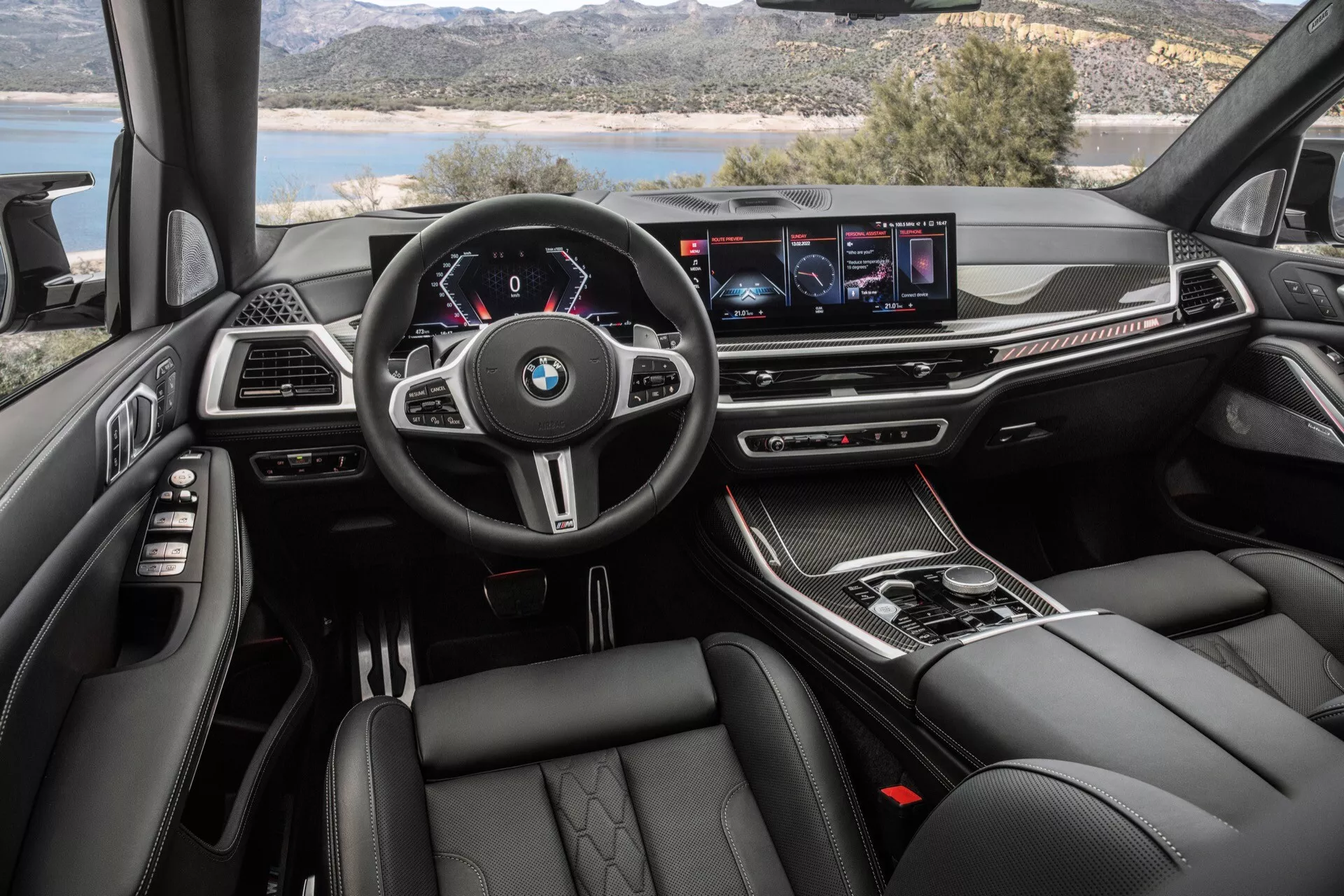 Interiörvy av BMW X7 2022 (G07 Ansiktslyft) ur förarens perspektiv med multifunktionsratt med BMW-logga, digital instrumentpanel, widescreen infotainment display, klimatkontrollknappar, automatisk växelväljare, lyxiga material, sportiga och bekväma säten, samt stämningsbelysning