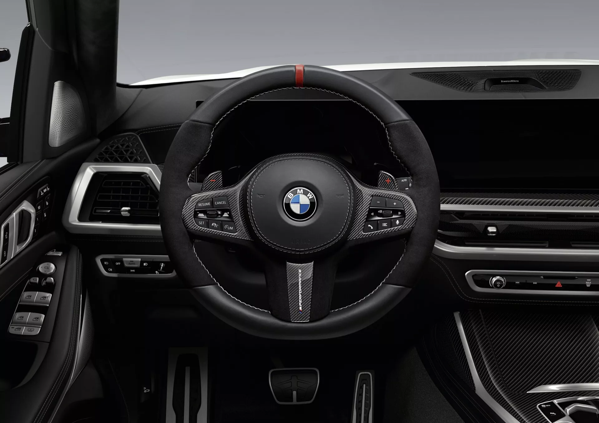 Interiör av BMW X7 2022 (G07-Facelift) med fokus på den sportiga, svarta läderomslutna ratten med röd markering, multifunktionsknappar och paddlar bakom ratten mot en sofistikerad instrumentbräda med eleganta luftventiler, krom- och kolfiberliknande texturer