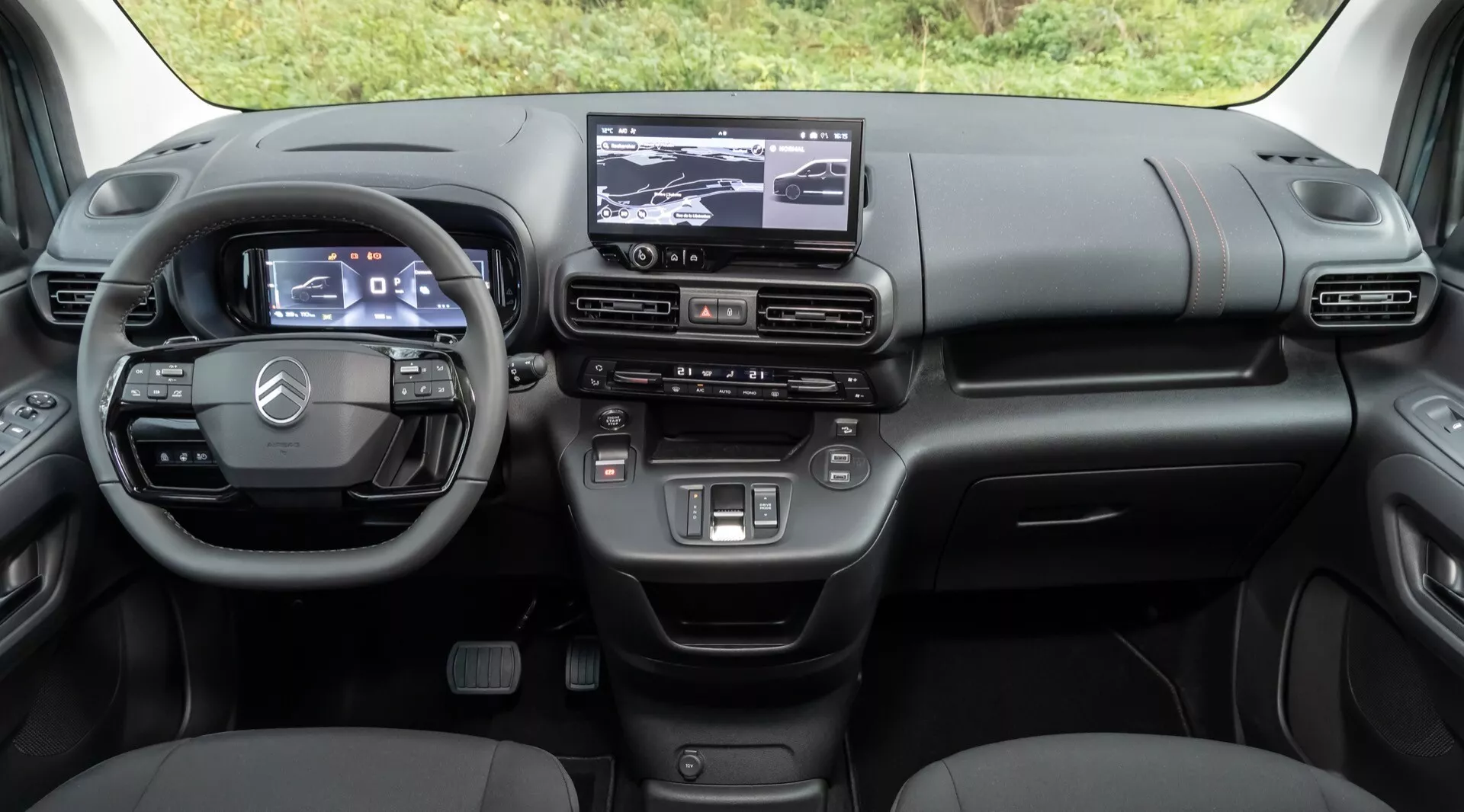 Interiör vy av Citroen Berlingo 3:e generationens facelift 2024 med avancerad digital instrumentbräda, trespaksratt med integrerade kontroller, pekskärmsinfotainmentsystem, och detaljerat klimatkontrollsystem från baksätets perspektiv