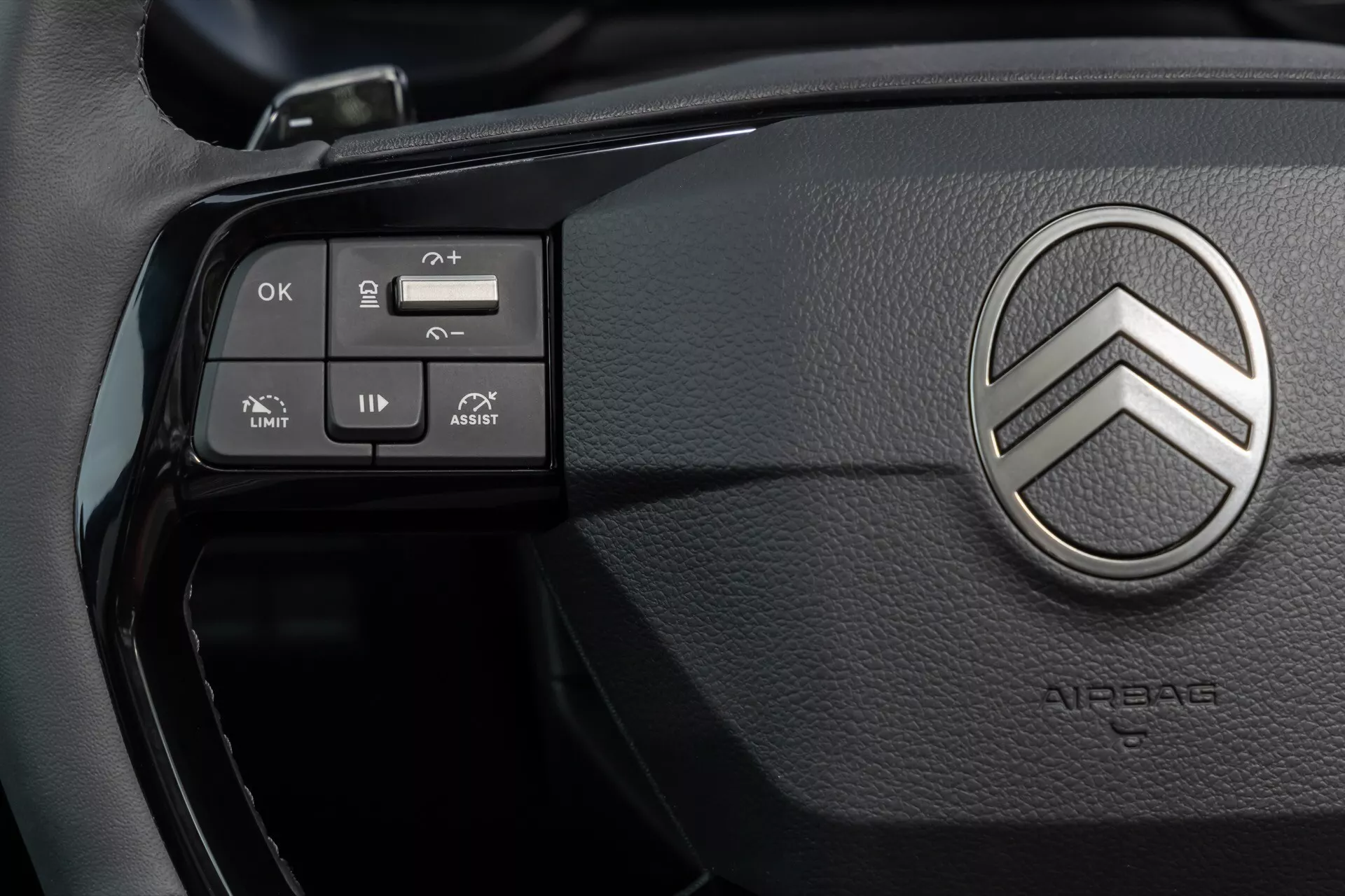 Närbild av ratten på Citroën Berlingo 2024 (3:e generationens ansiktslyft) med metallisk dubbel-chevron emblem, kontrollknappar för farthållare, ljud, menynavigering och körhjälpmedel som hastighetsbegränsare och filhållningsassistans