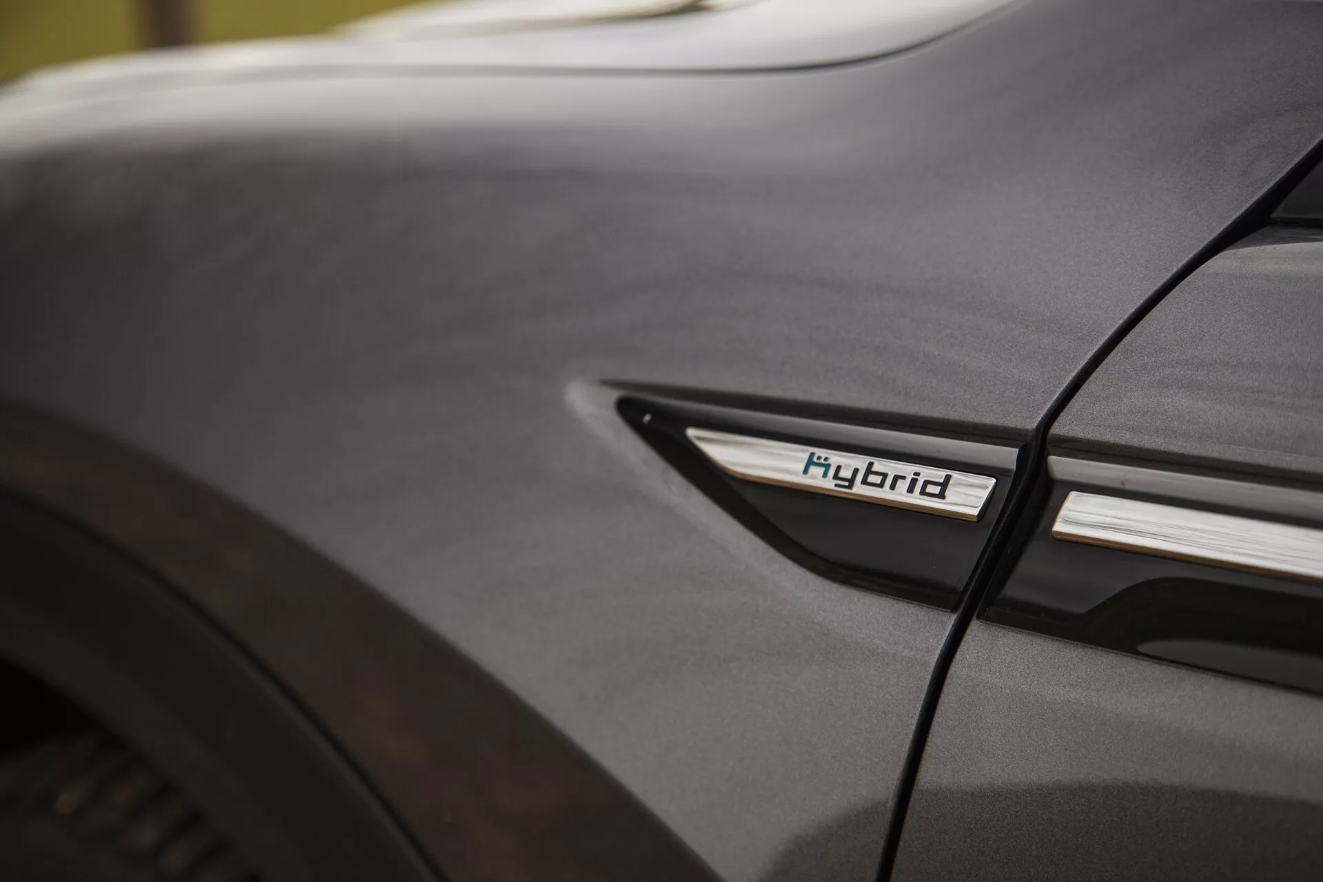 Närbildsdetalj av Citroen C5-X 2022 med hybridemblem på den nedre sidoprofilen nära bakhjulsbrunnen, som visar hybridteknik och designestetik under mjuka ljusförhållanden