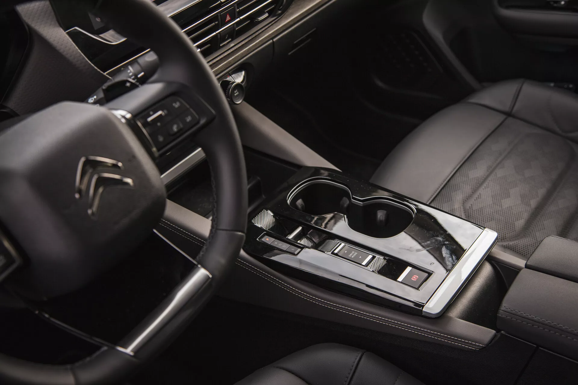 Interiörvy av Citroën C5-X 2022 som visar multifunktionsratten med logotyp, högteknologisk instrumentbräda med infotainmentsystem, snygg automatisk växelspak, klimatkontroll, läderklädda säten med kvalitetssöm och en touch av livsstil med solglasögon på den glansiga centrala ytan