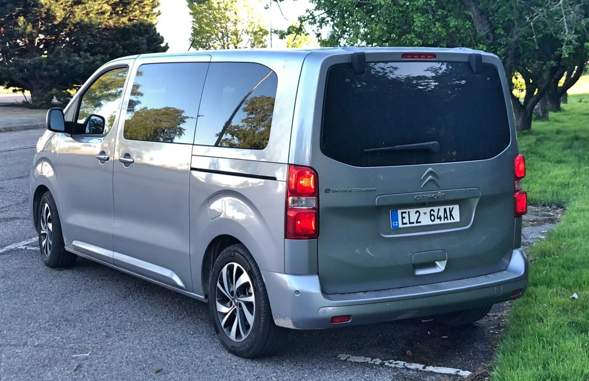 Citroën Spacetourer 2016 fångad från en trekvarts bakre vinkel, vilket framhäver den högra bakre sidan med baklucka, bakrutedefroster, bakre vindrutetorkare, dubbla bakljus, centralt monterad registreringsskylt, skjutbar sidodörr, bakre fönster som kan indikera ytterligare sittplatser, och silvermålade multifalgsfälgar; parkerad på en förorts- eller park-liknande gata med tydliga träd och gräs.