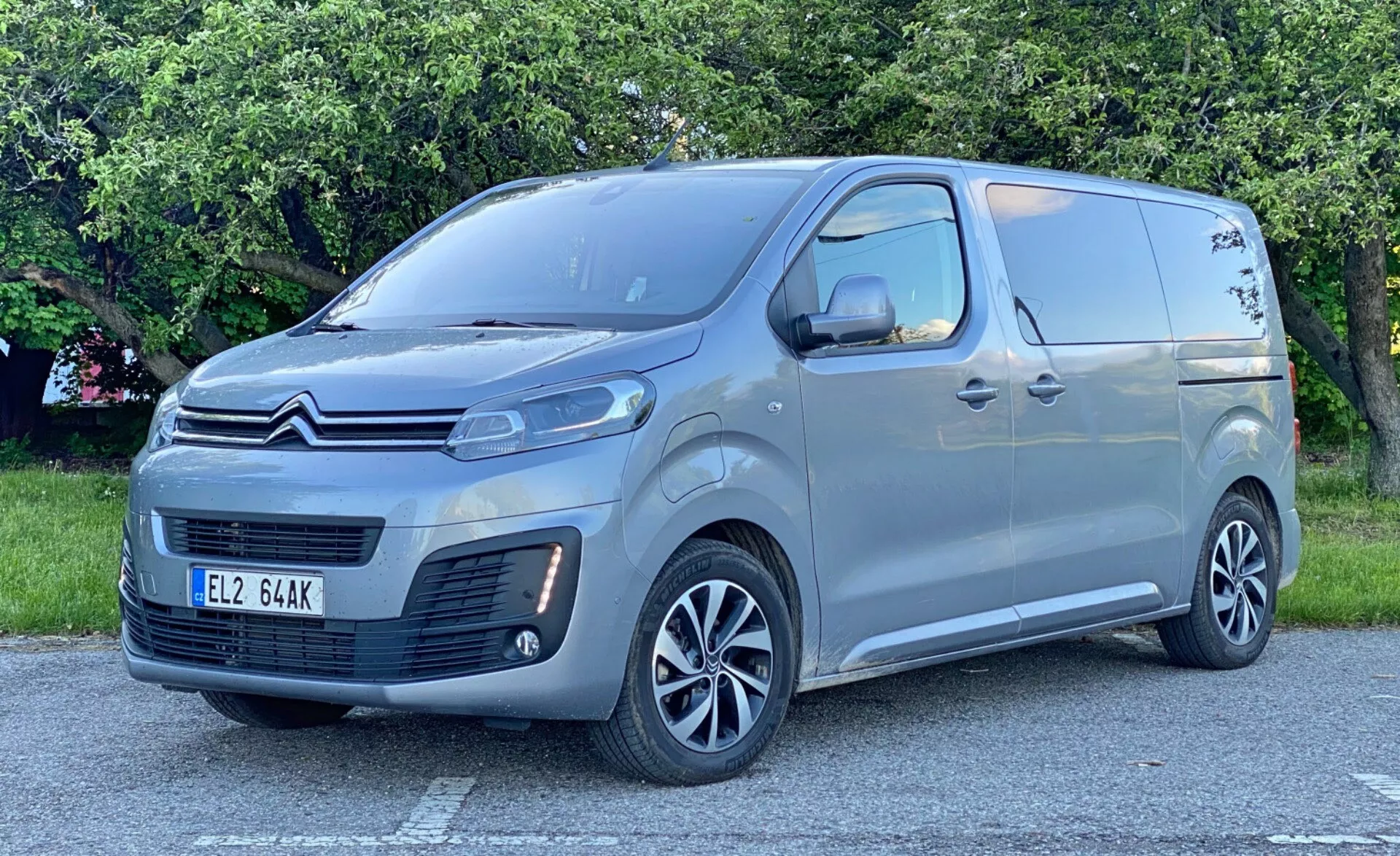 2016 års Citroen Spacetourer skåpbil i lugn utomhusmiljö, trekvarts frontvy som visar framgrillen med distinkt mönster och märkeslogotyp, eleganta LED-strålkastare, främre stötfångare med dimljus och luftintag, skjutdörrar med integrerat sidosteg, passagerarfönster bakom framdörrarna, moderna fälgar i legering med flera ekrar, metalliclack, stora sidospeglar med integrerade blinkers, subtila linjer längs sidopanelen.
