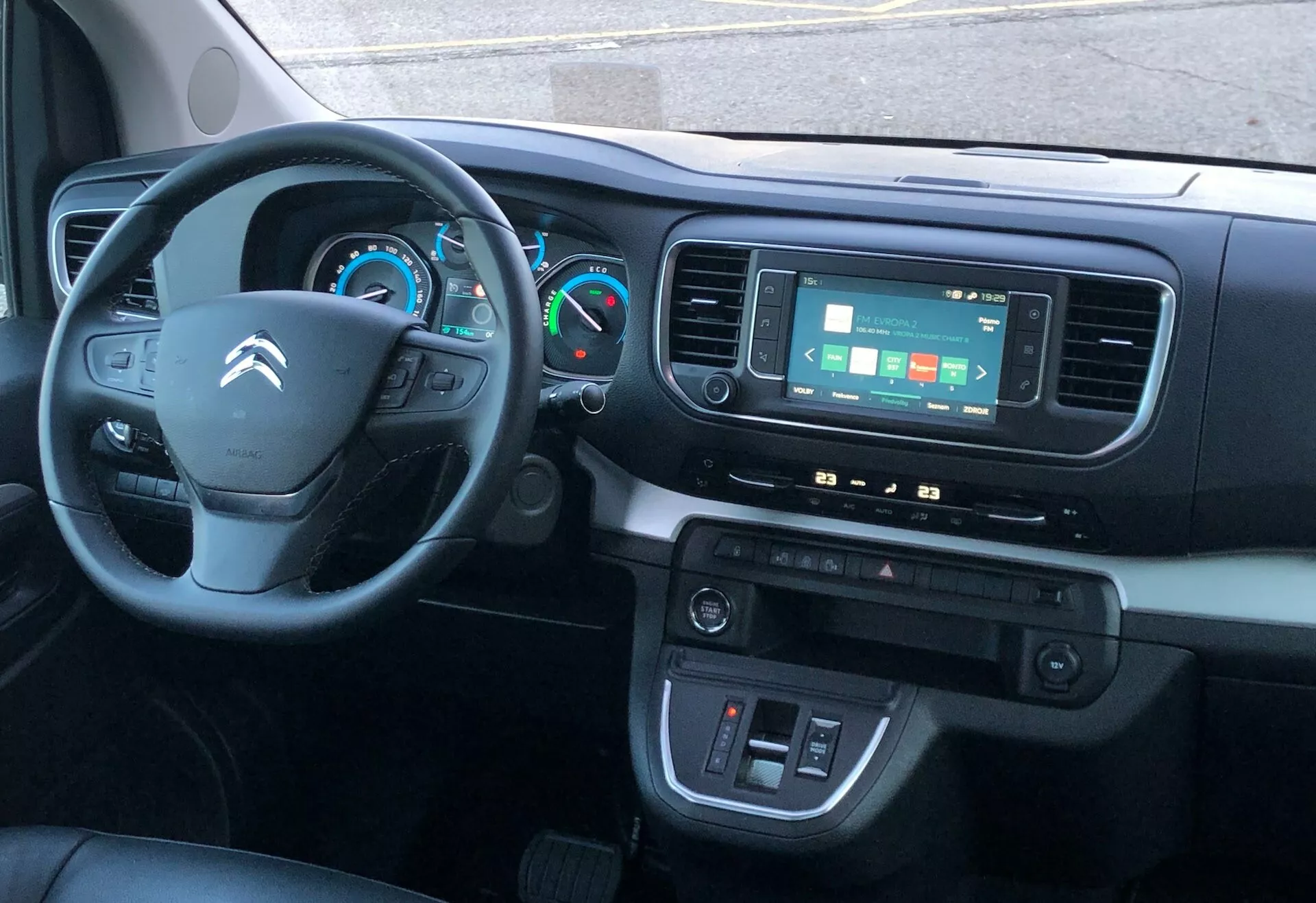 Interiörvy av en Citroën SpaceTourer 2016 från framsätet på passagerarsidan, som visar instrumentbrädan, en treekrad ratt med kontroller, delvis synligt instrumentkluster med analoga och digitala displayer, pekskärmsinfotainmentsystem, klimatreglage och förardörr med kontroller för fönster och sidospeglar. Mittkonsolen inkluderar troligtvis förvaringsutrymme och hjälportar.