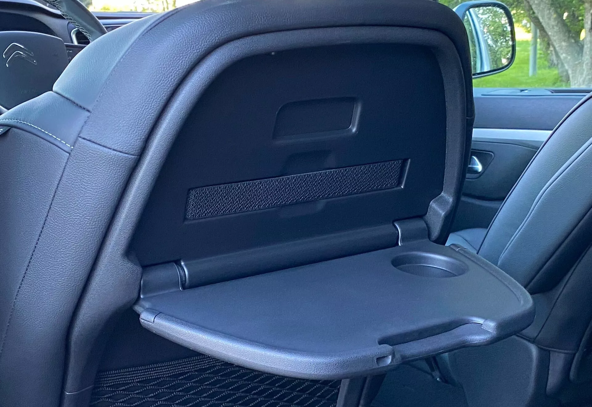 Närbild av interiören i Citroen Spacetourer 2016, fokuserad på baksidan av ett mörkt lädersäte framifrån från ett baksätesperspektiv. Sätet har ett infällbart armstöd med en grund urholkning för mugghållare och ett litet förvaringsutrymme under ett fällbart lock. Ovanför finns en rektangulär förvaringsficka med ett nät för att hålla föremål på plats. Bilden framhäver den förstklassiga kvaliteten med kontrasterande sömmar längs med sömmarna, fångad under goda ljusförhållanden.