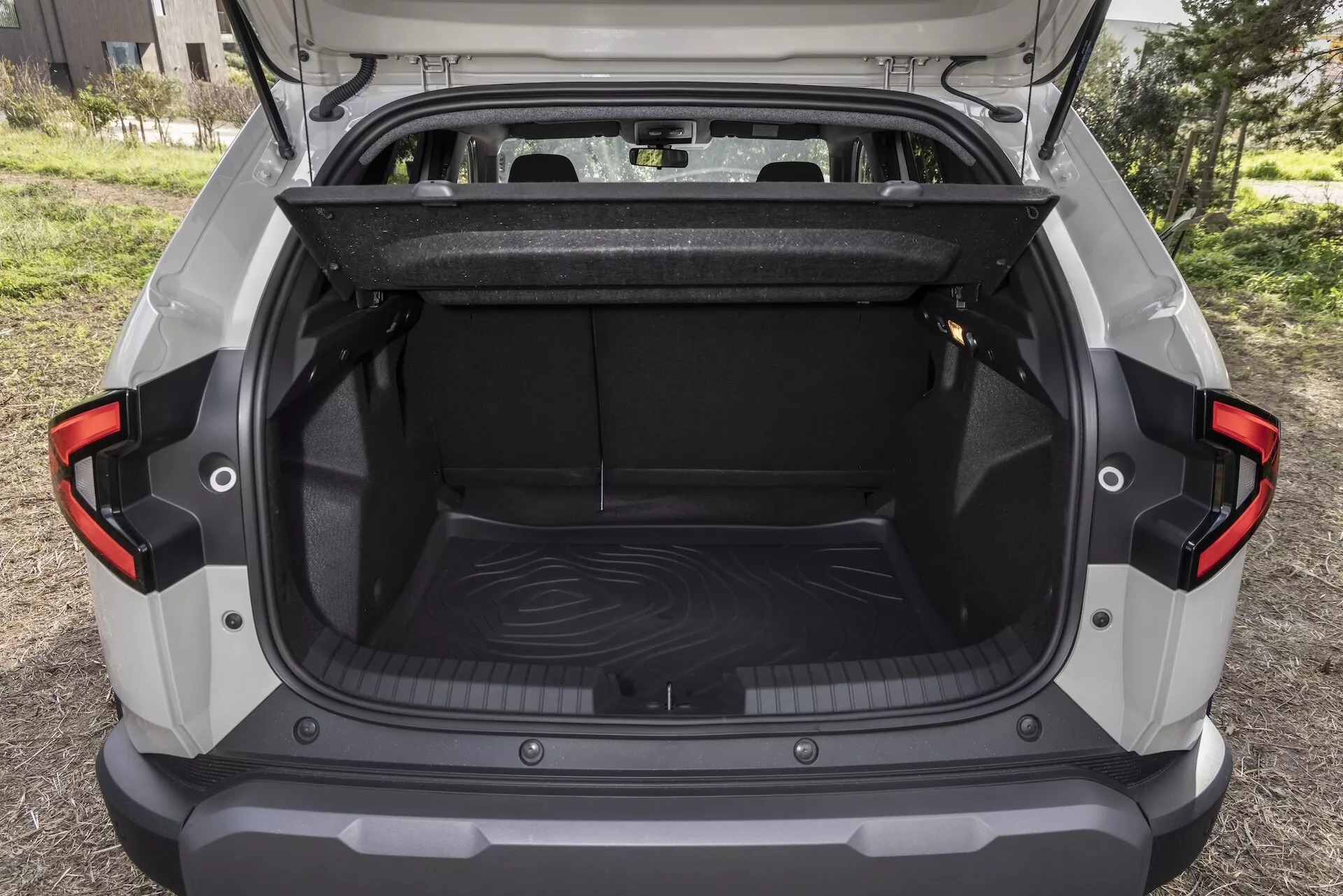 Dacia Duster 3:e generationen 2024 med öppen bagageutrymme som visar rymligt lastutrymme, skyddsmatta och moderna LED-bakljus, mot en utomhusbakgrund, vilket framhäver praktikalitet och design