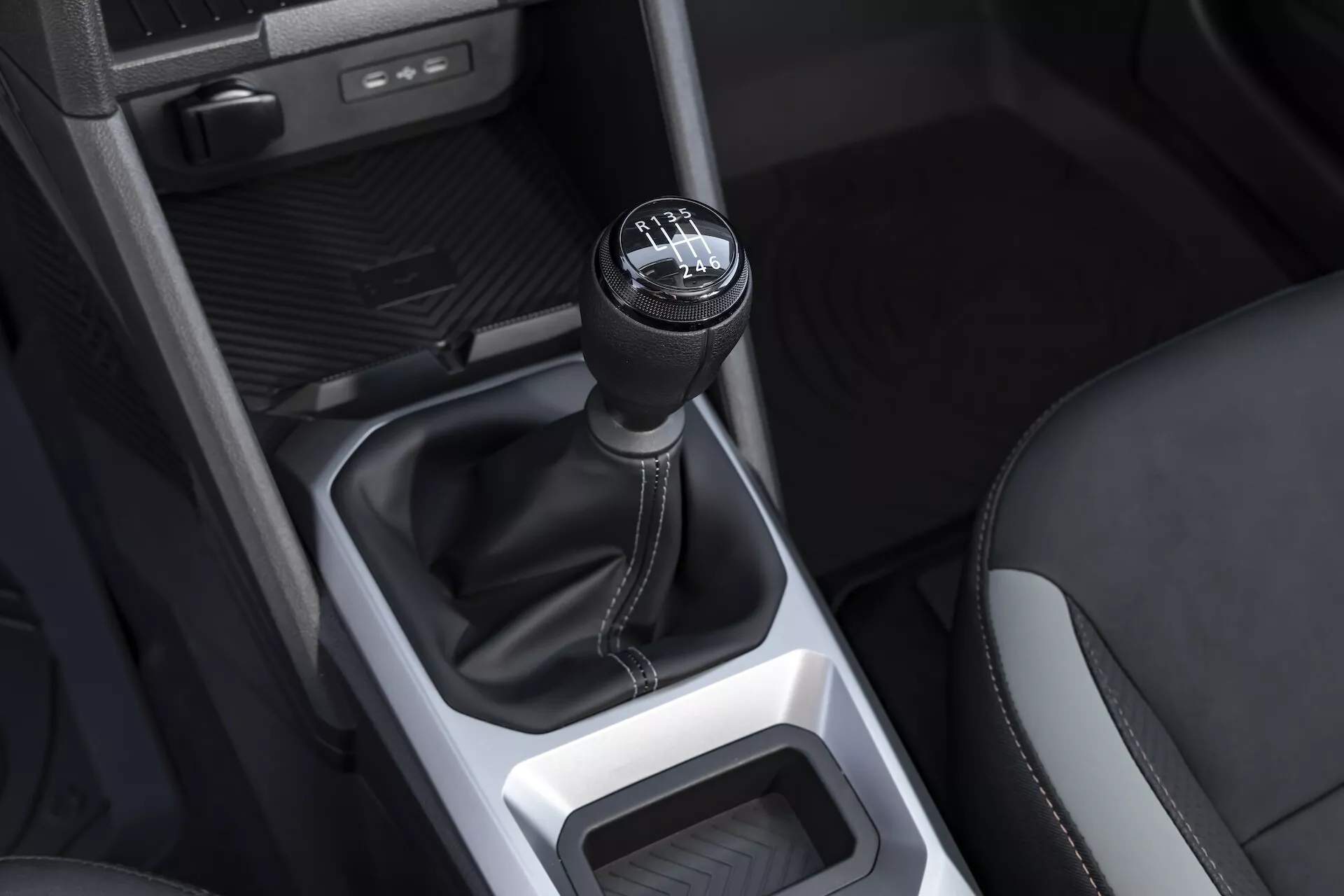 Närbild av växelspaksområdet för Dacia Duster 3:e generationen 2024, visar en växelspaksknopp för manuell växellåda av hög kvalitet med emblem, läderstövel och minimalistisk konsoldesign.