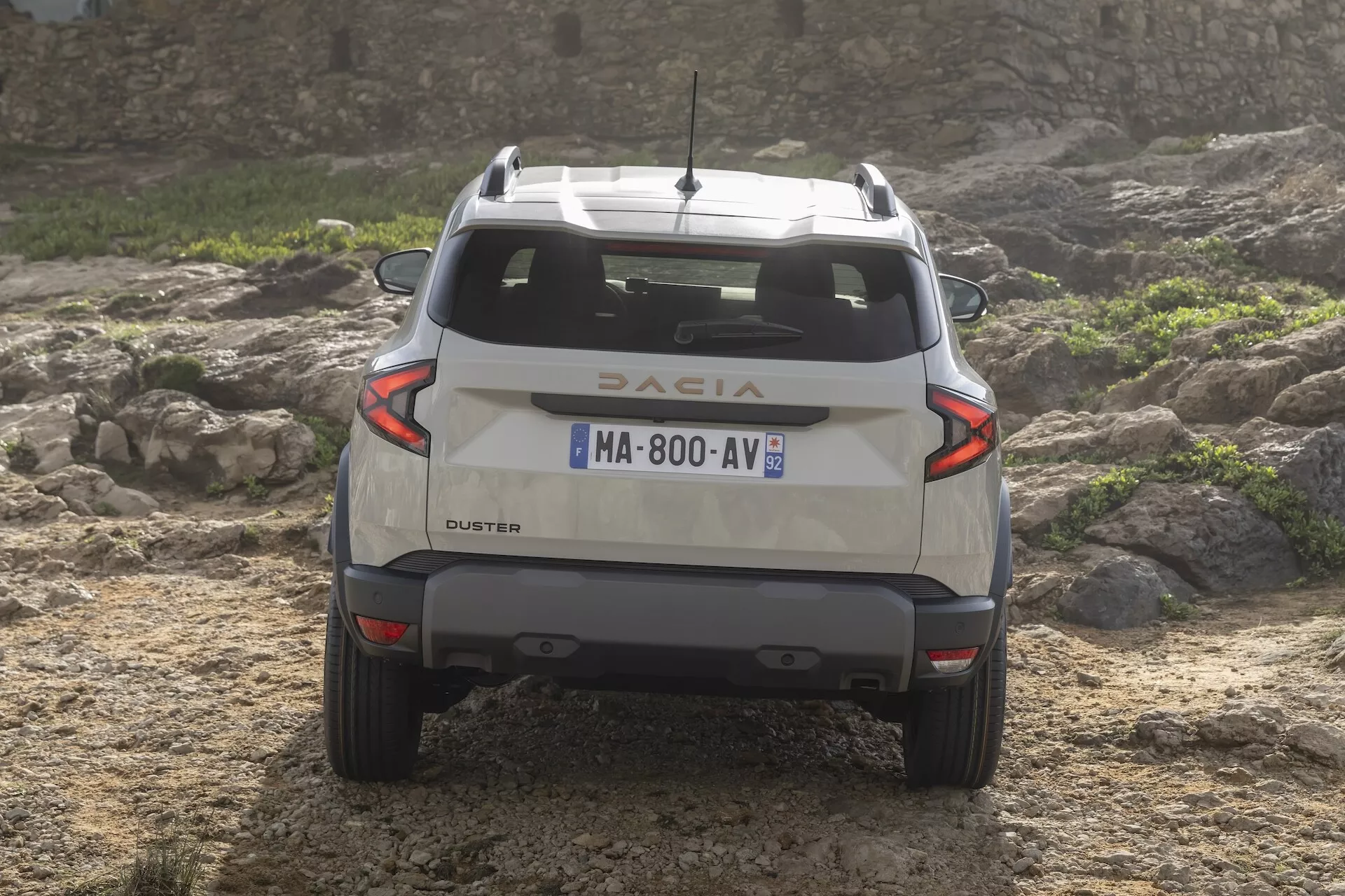 Baksida av tredje generationens Dacia Duster 2024 på ojämnt terräng som visar exteriördesign, LED bakljus, takräcken, legeringshjul och terrängkapacitet