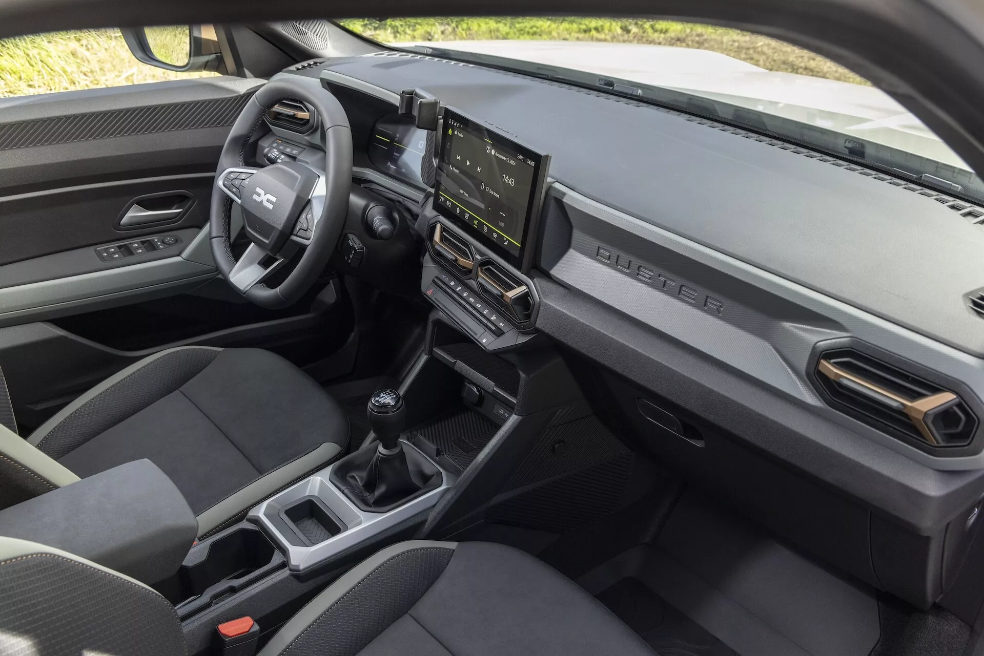 Interiör vy av Dacia Duster 3:e generationen 2024 som visar instrumentbrädan, mittkonsolen och det främre passagerarområdet med multifunktionsratt, pekskärmsinfotainmentsystem och växelspak för manuell växellåda