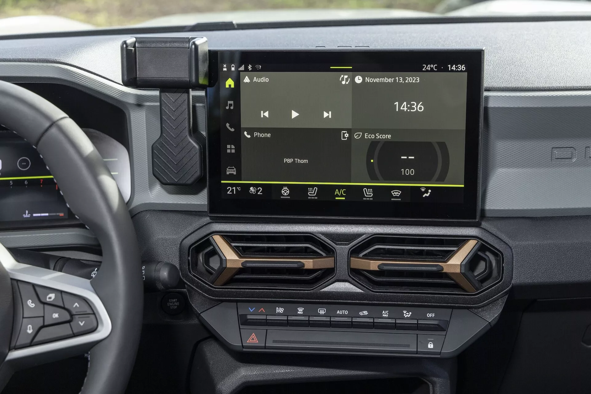 Interiör av Dacia Duster 3:e generationen 2024 med fokus på det centrala instrumentbrädan: pekskärmsinfotainmentsystem som visar ljudkontroller, tid och temperatur, eleganta luftventiler, ratt med monterade kontroller och knappar för klimatkomfort
